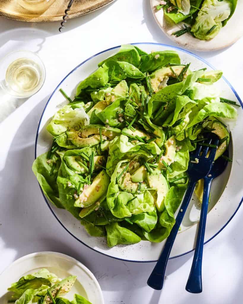 A plate with butter lettuce salad, along with a fork and spoon to serve, and two small plates with the salad served in them.