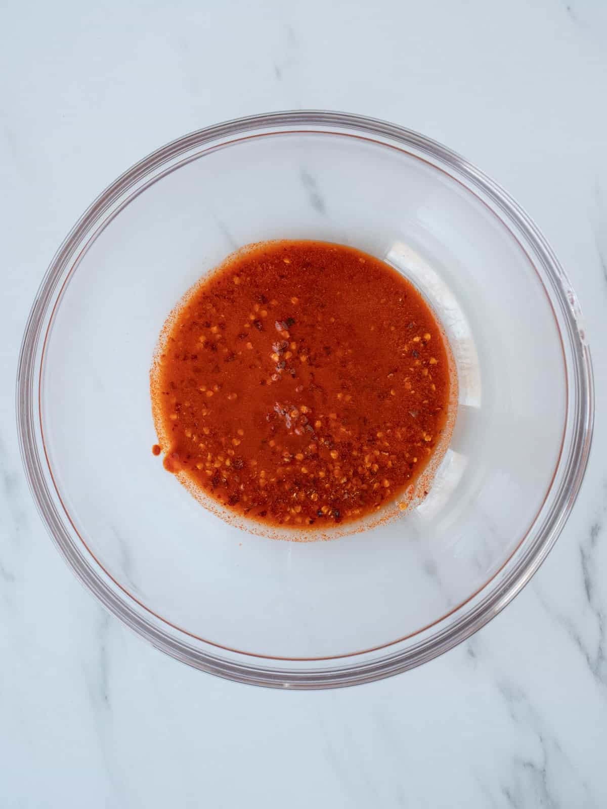 A large glass mixing bowl with crushed red pepper and paprika mixed with some hot water.