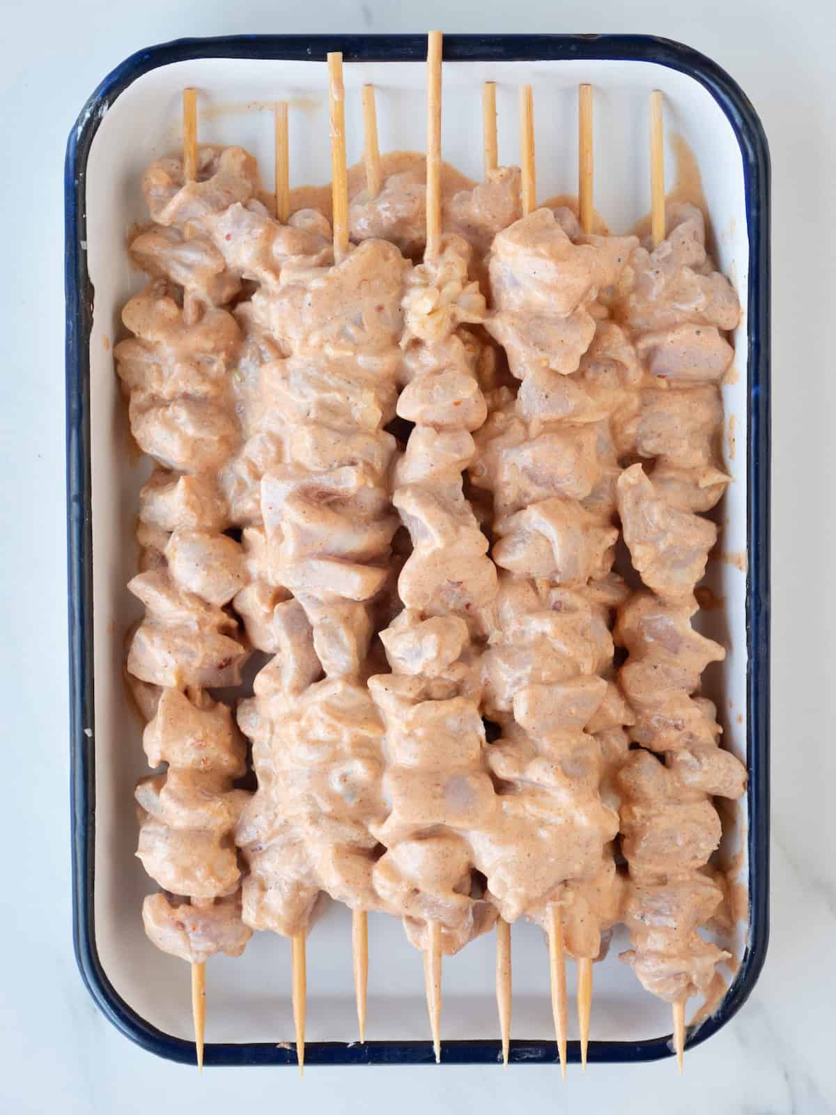 A rectangular dish with wooden skewers with the marinated chicken cubes threaded on them.