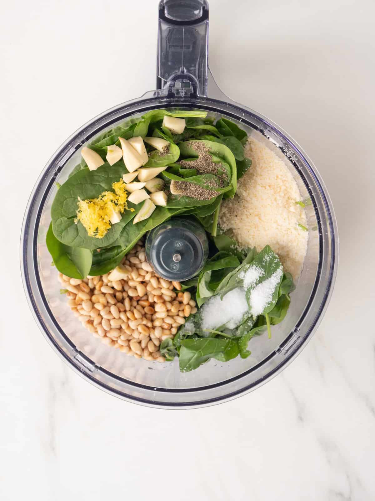 An overhead shot of a food processor jar with all the ingredients to make basil pesto ready to be blended.