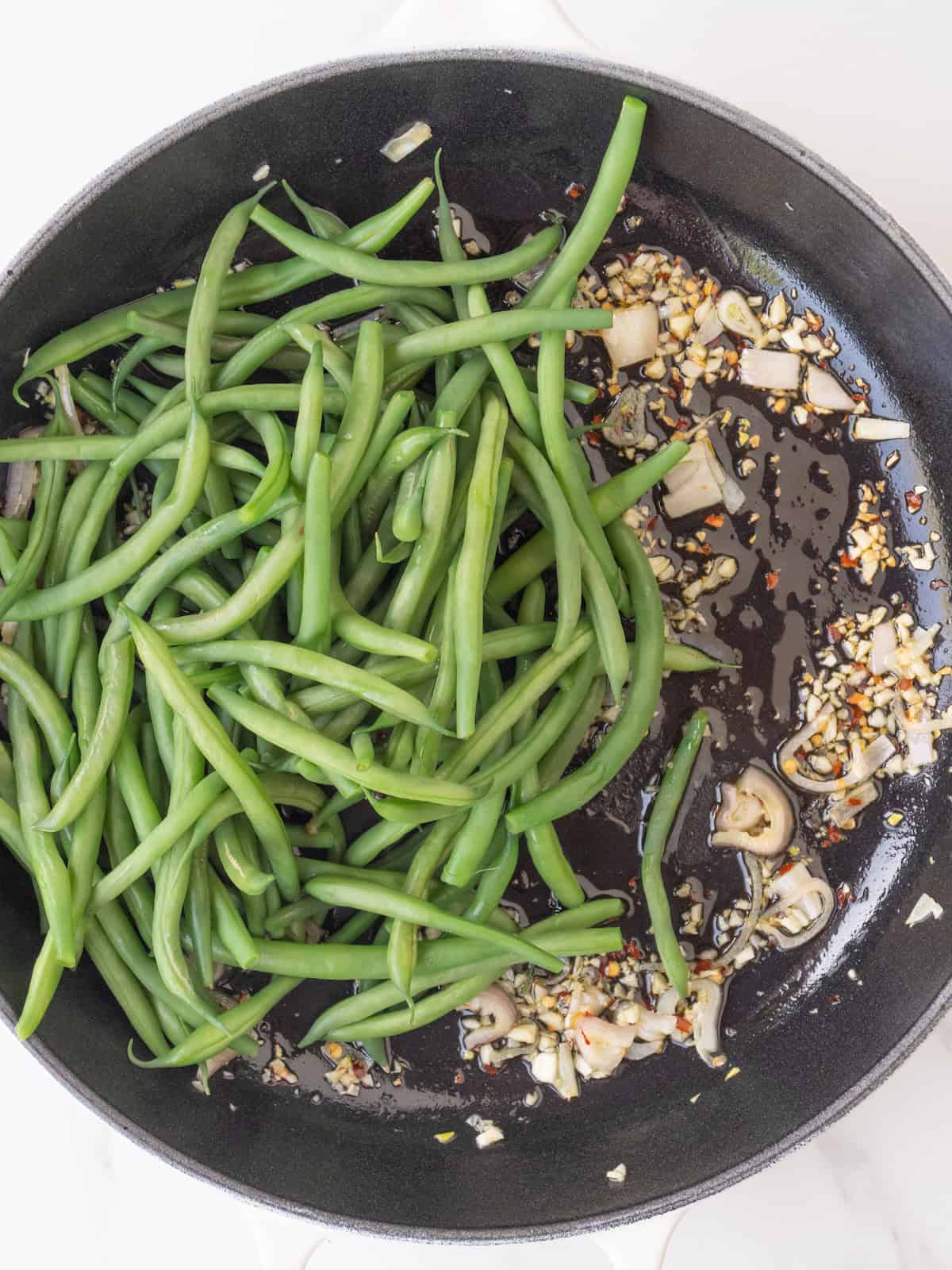 A skillet with sautéed shallots, garlic and red pepper flakes and boiled green beans just added.