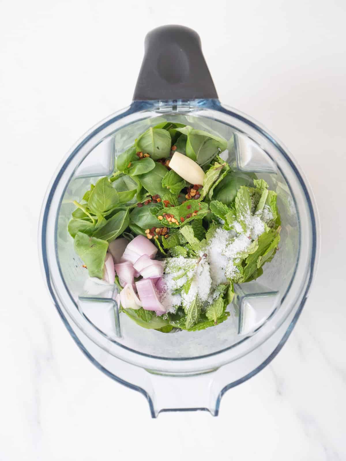A jar of a blender with all the ingredients to make mint basil vinaigrette.