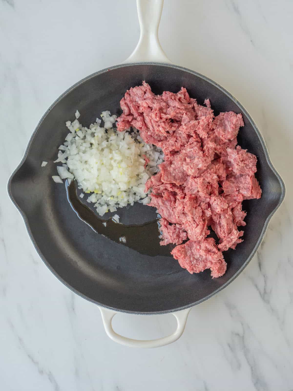 A skillet with onions being sautéed in olive oil and ground beef added.