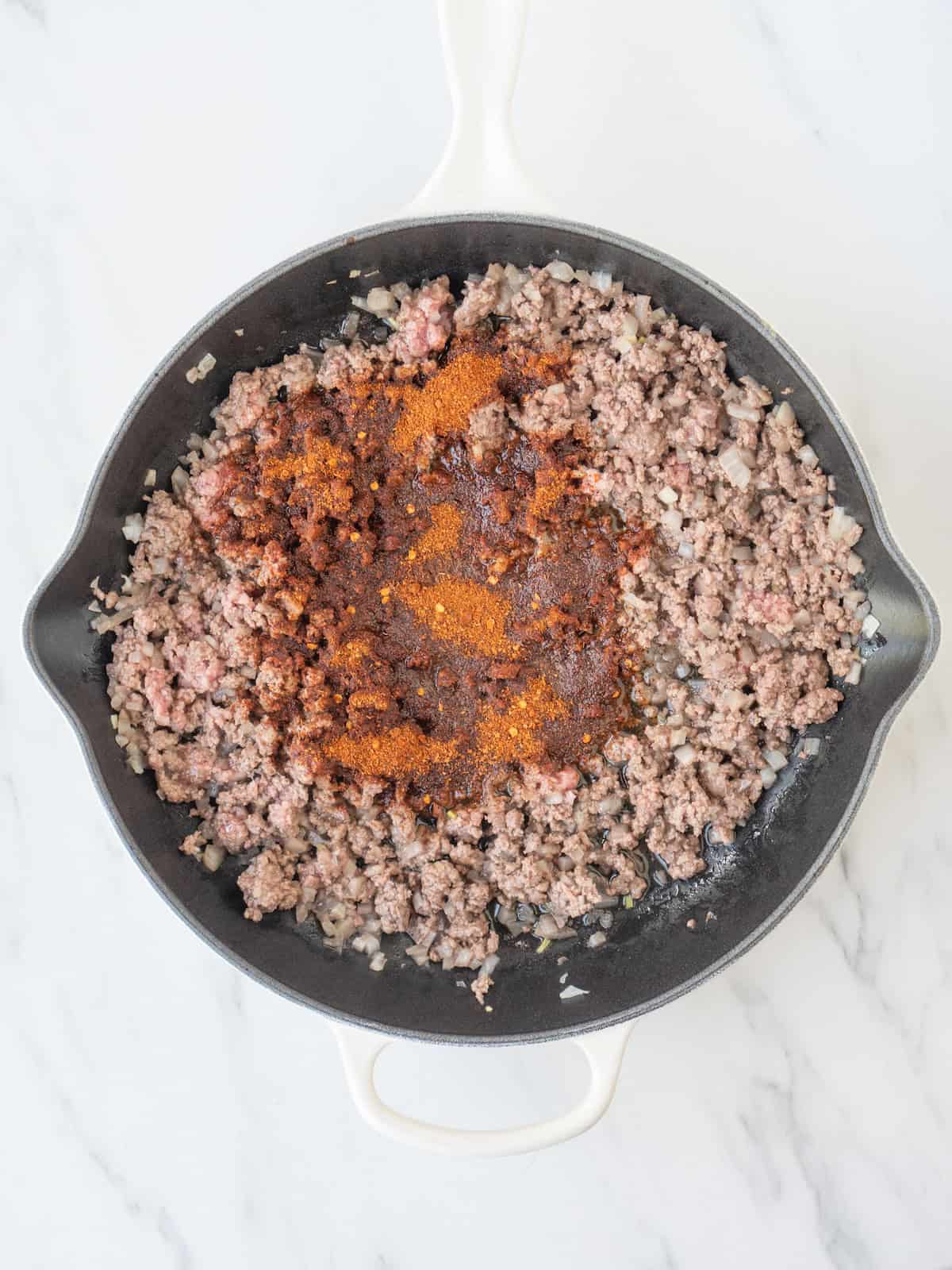 A skillet with ground beef being cooked and taco seasoning added.