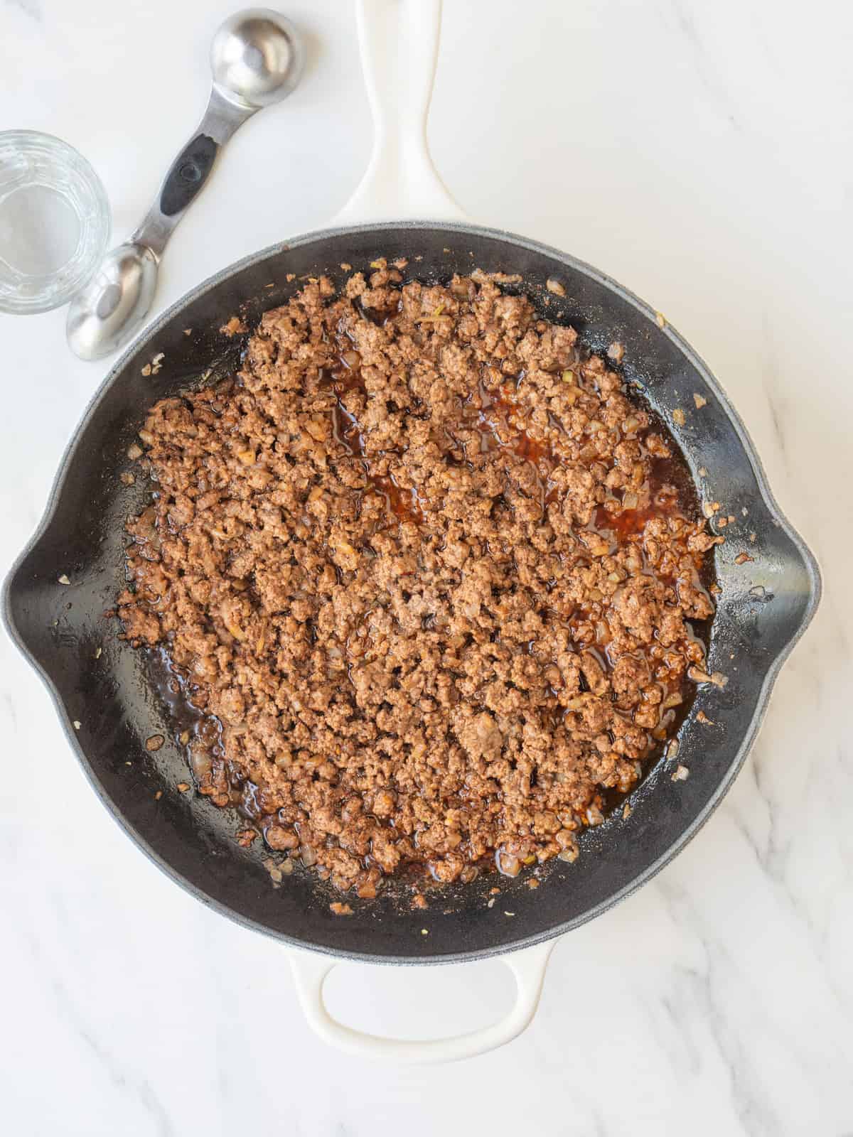 A skillet with ground beef being cooked and water added.