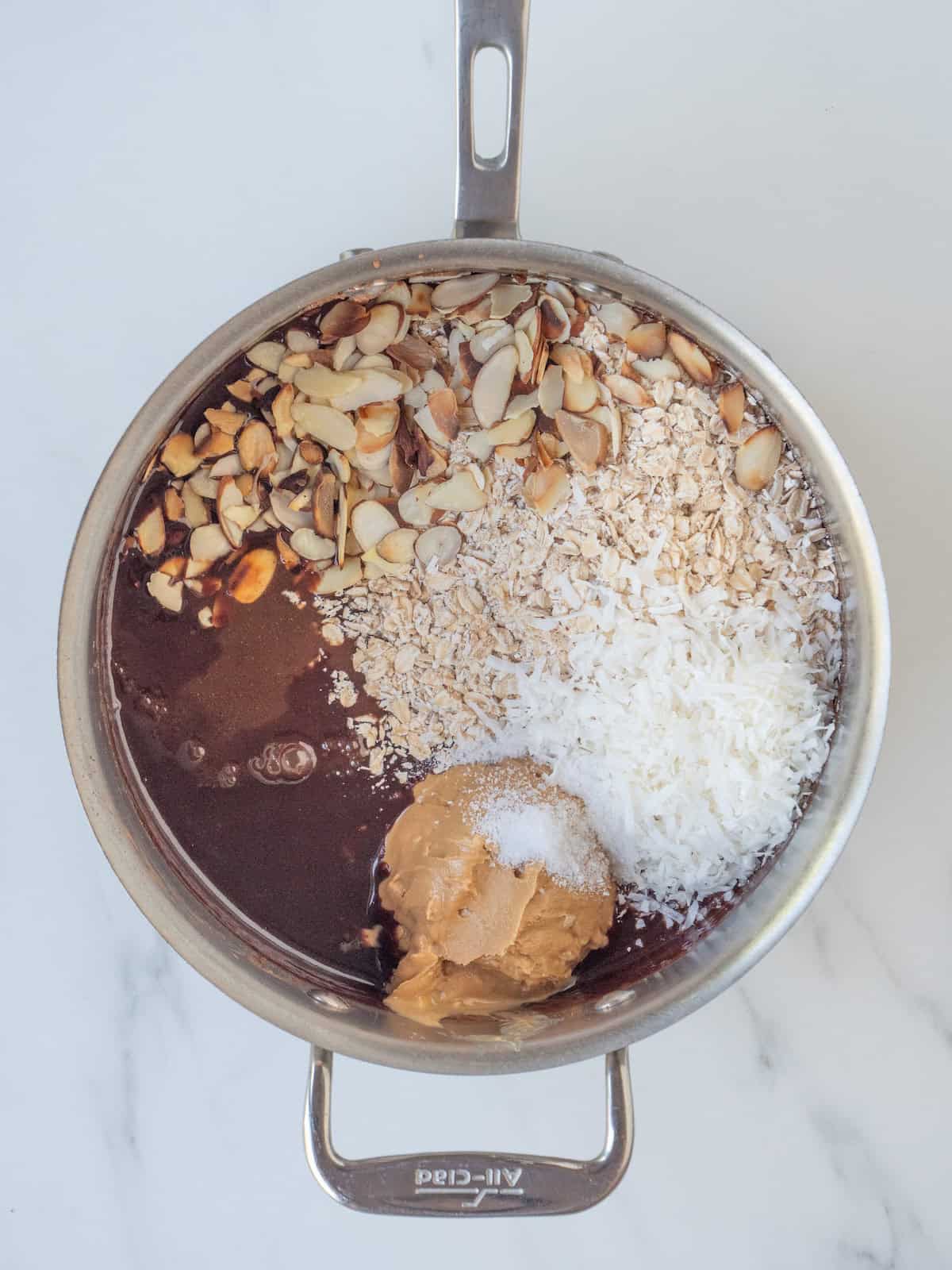 A skillet with the wet ingredient mix warmed together with almond butter, vanilla, salt, oats, almonds and coconut added.