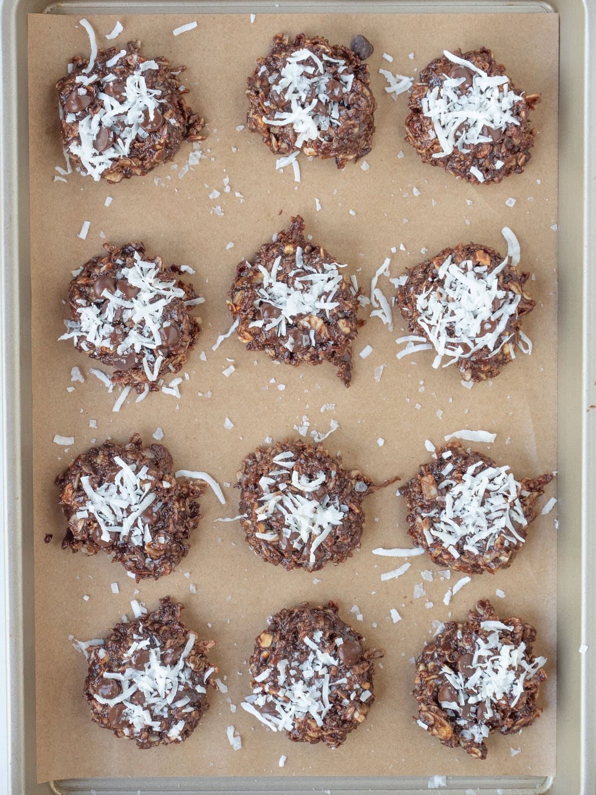 An overhead shot of a baking sheet lined with parchment paper with no bake Double Chocolate Chip Cookies with almond butter and coconut flakes.