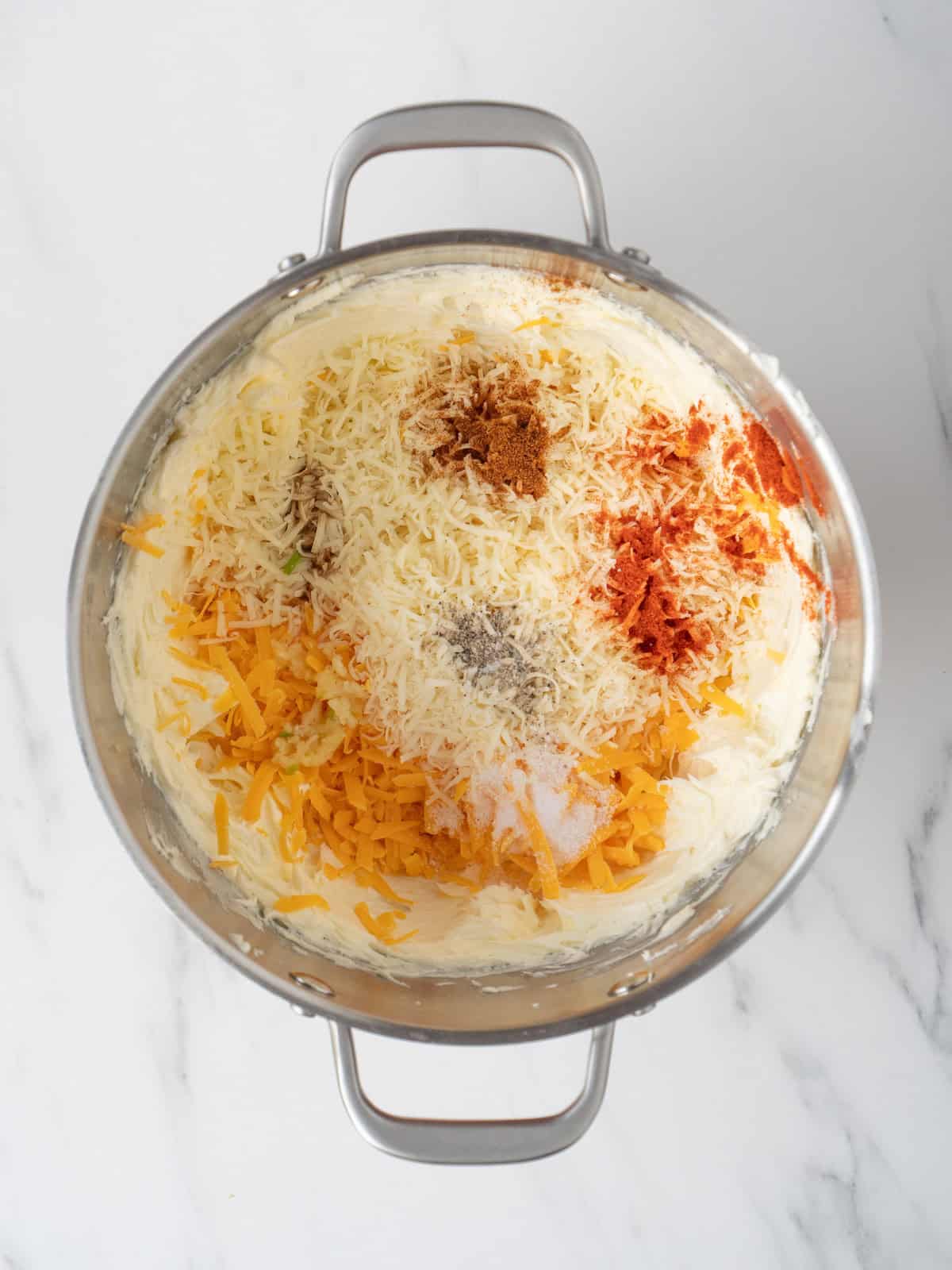 A stand mixer bowl with whipped room temperature butter, along with shredded cheddar, romano, garlic, worcestershire sauce, paprika, cayenne and salt added, ready to be whipped together to make garlic cheese butter.