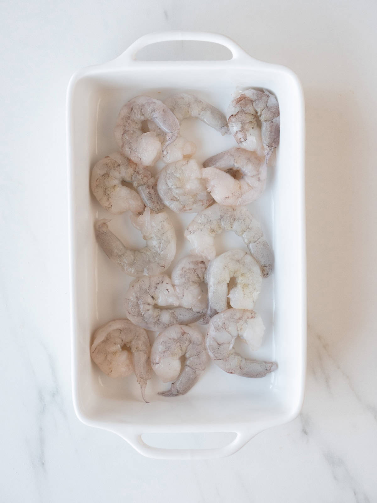 A baking dish with raw shrimp laid out to be marinated.