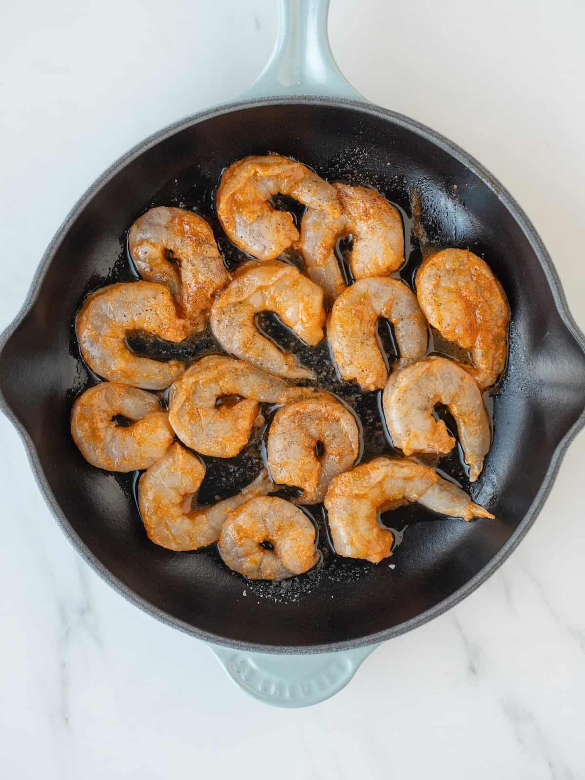 A large skillet with olive oil and shrimp being cooked.