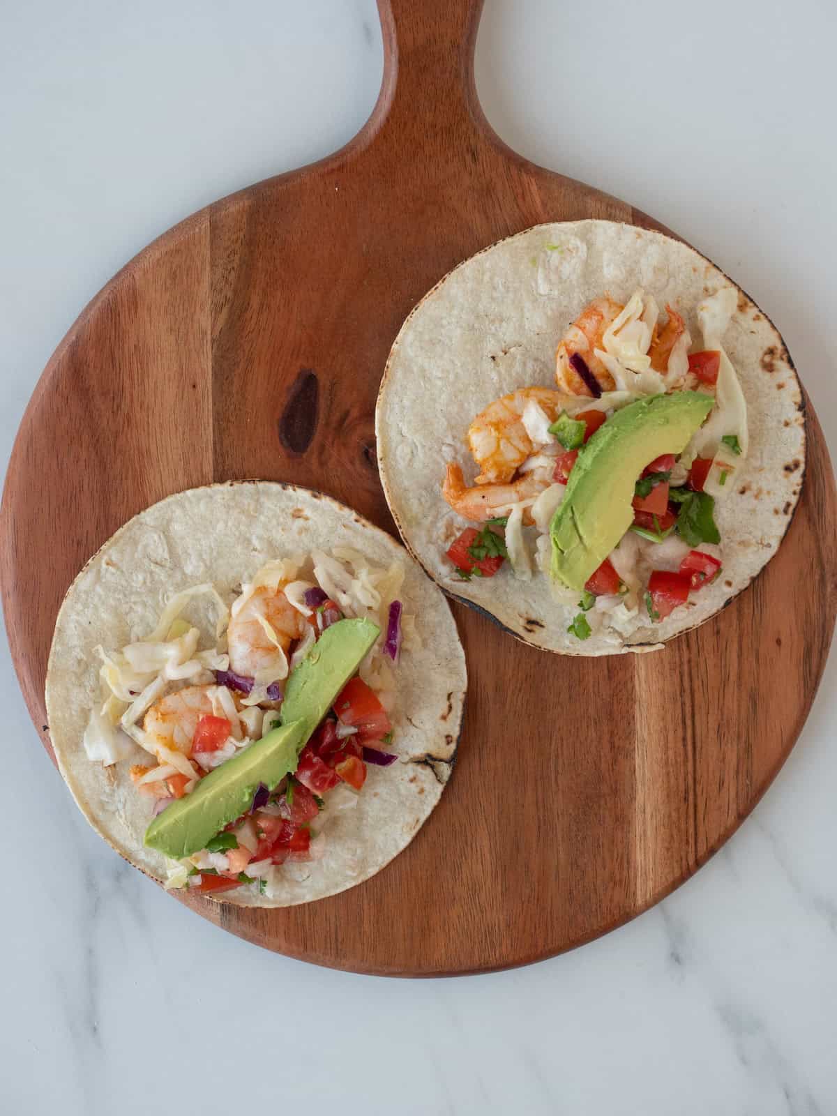 A wooden board with two shrimp tacos assembled and ready to be served.
