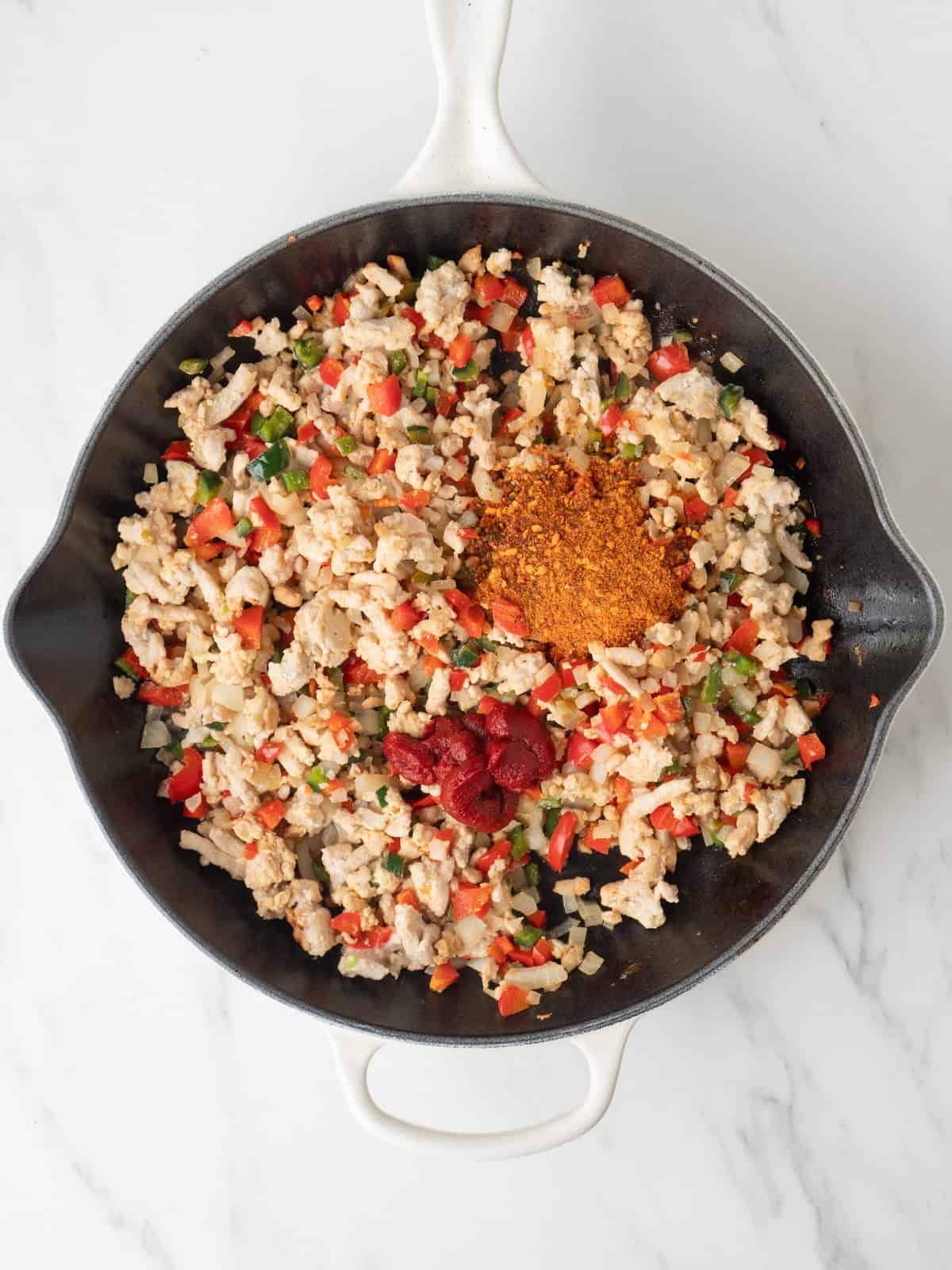 A skillet with ground turkey being cooked, and fajita seasoning just added along with tomato paste.