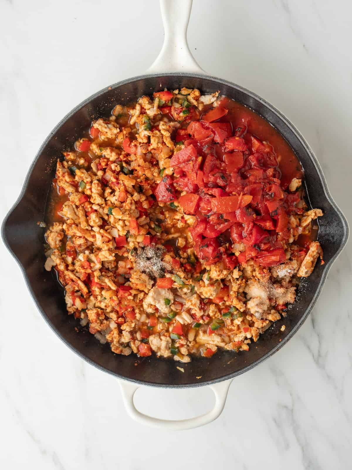 A skillet with ground turkey being cooked, and diced tomatoes, water and Worcestershire sauce just added.