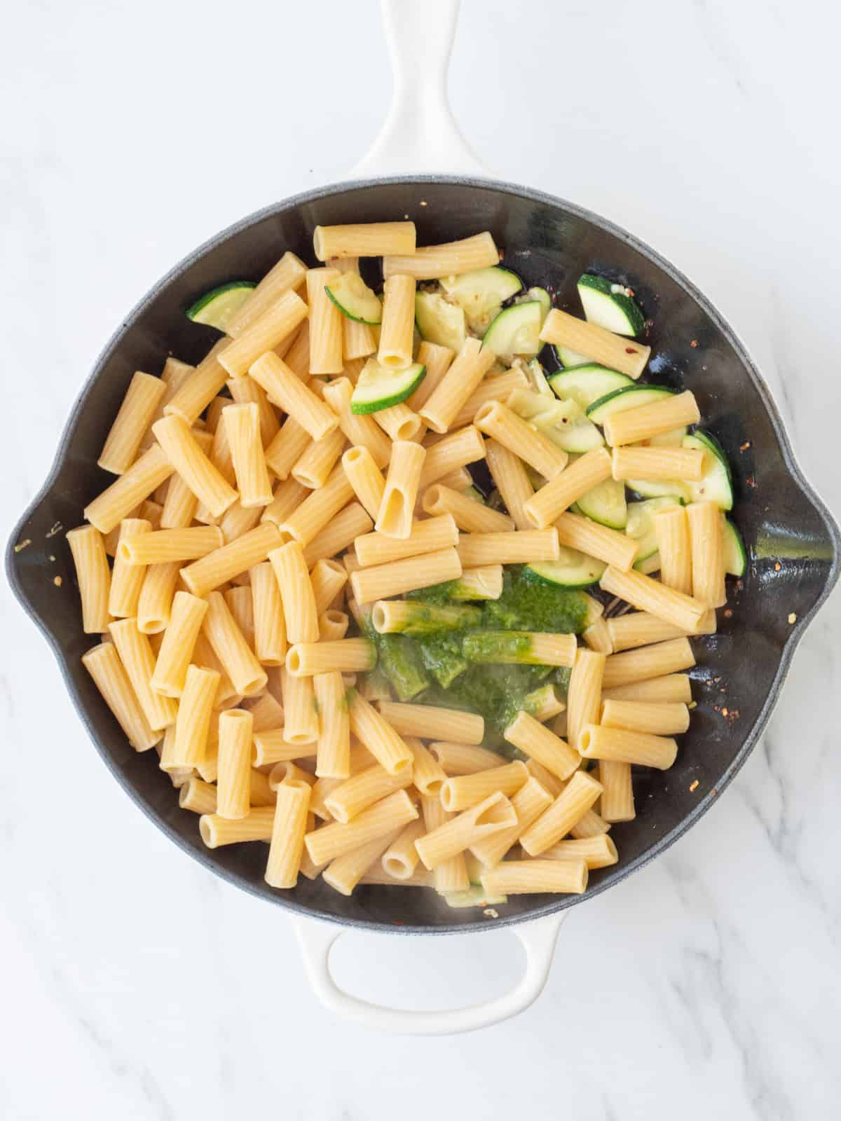 A skillet with sautéed zucchini, with pasta and basil vinaigrette added to it.