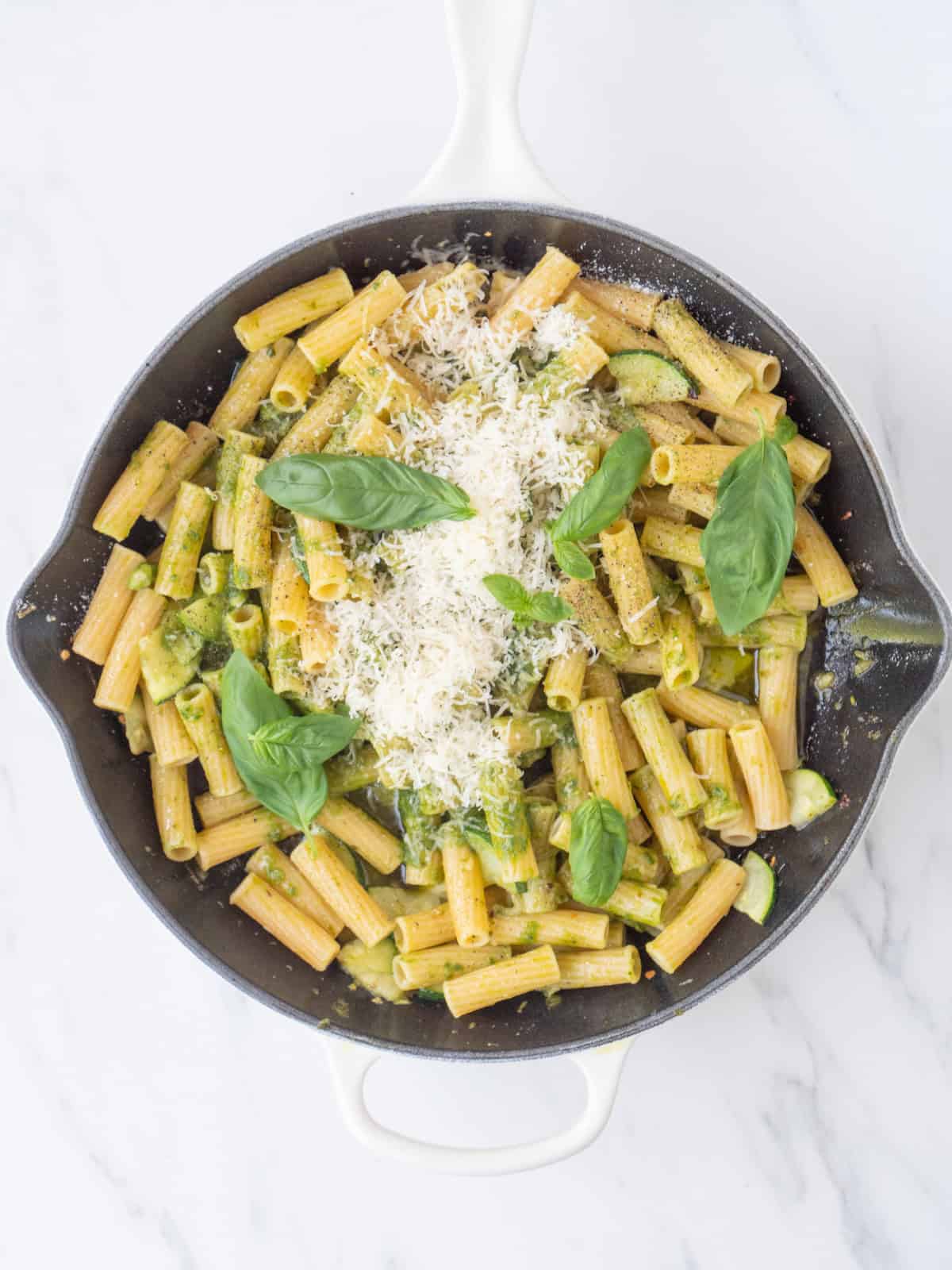 A skillet with basil vinaigrette pasta garnished with basil leaves and grated parmesan.