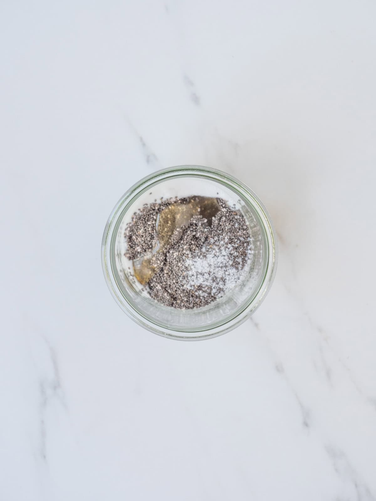 A mason jar with all the ingredients to make chia pudding, which are milks, chia seeds, honey and salt.