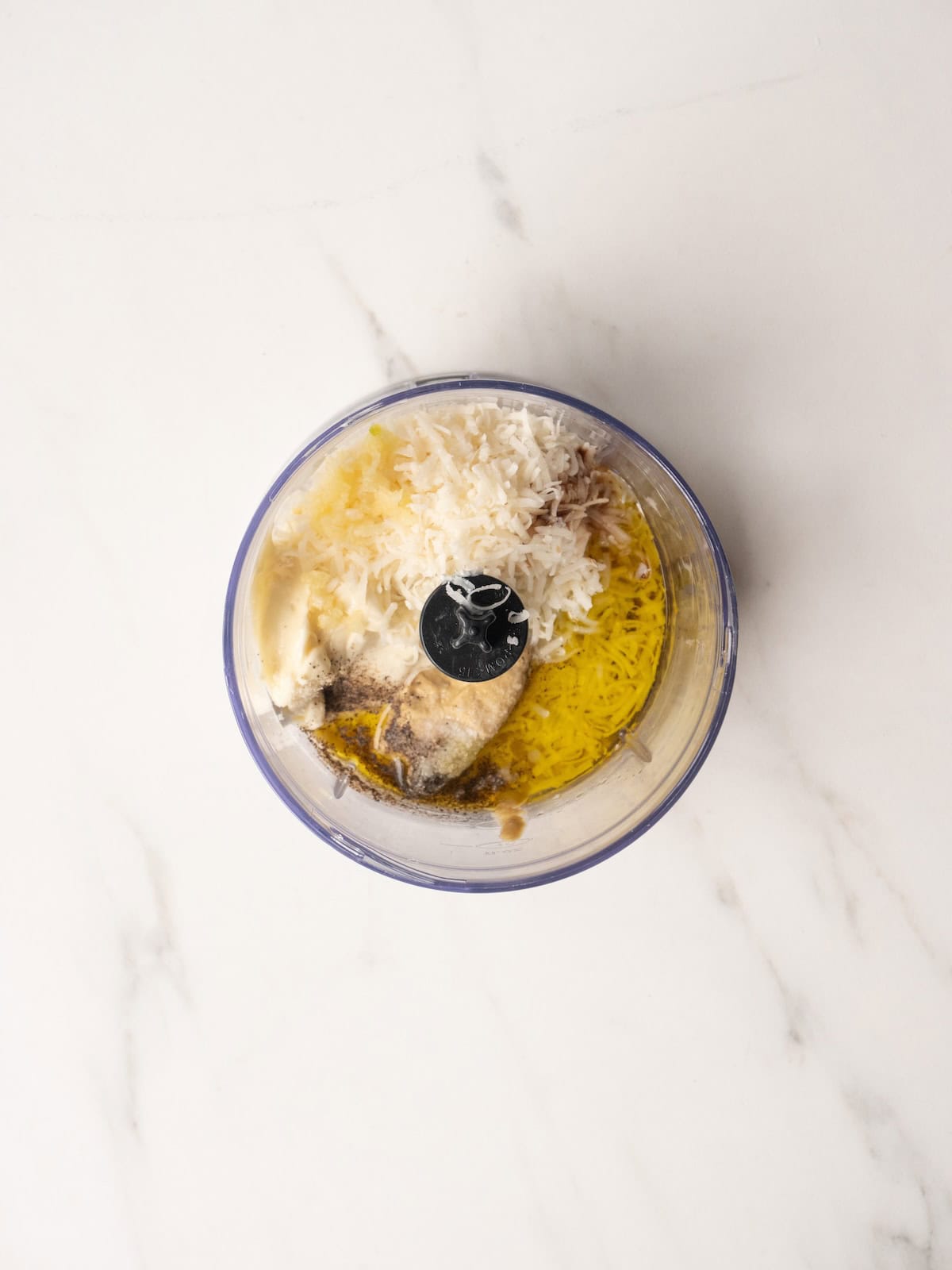 Food processor jar with all ingredients to make caesar salad dressing.