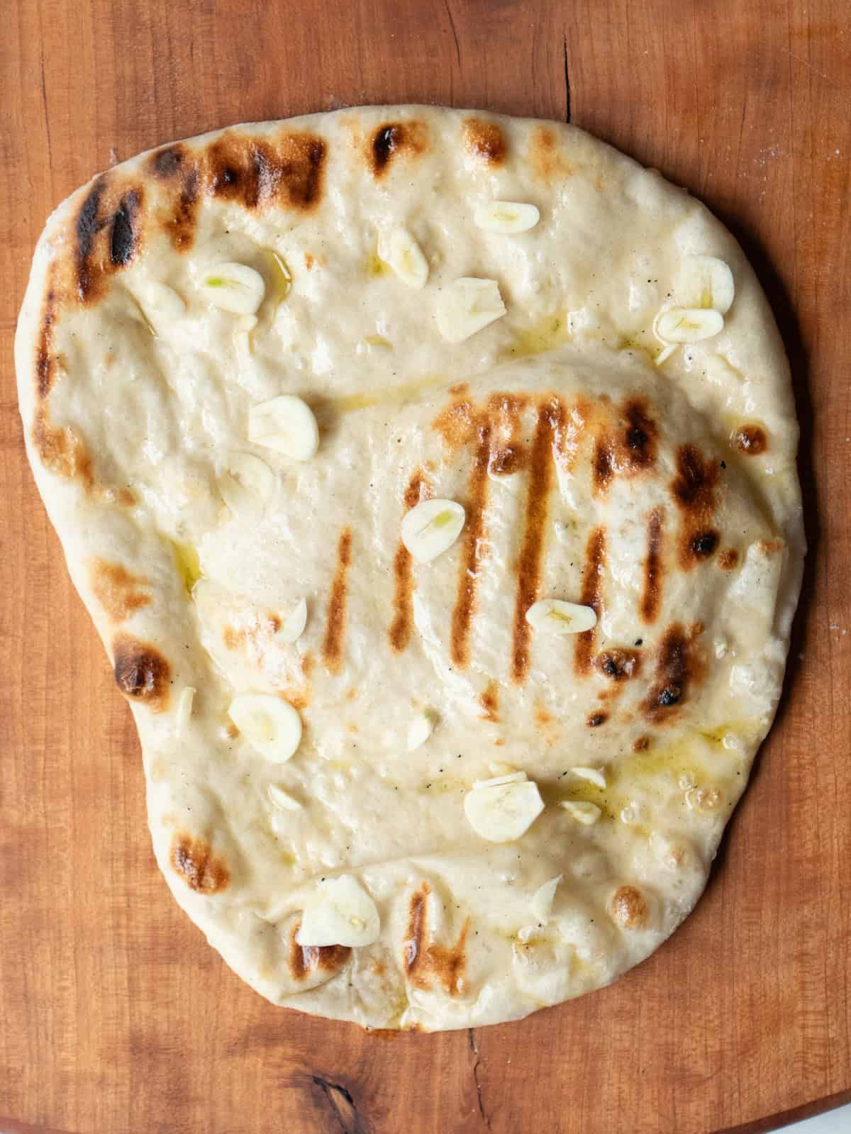 A freshly grilled pizza base brushed with olive oil and sprinkled with garlic.