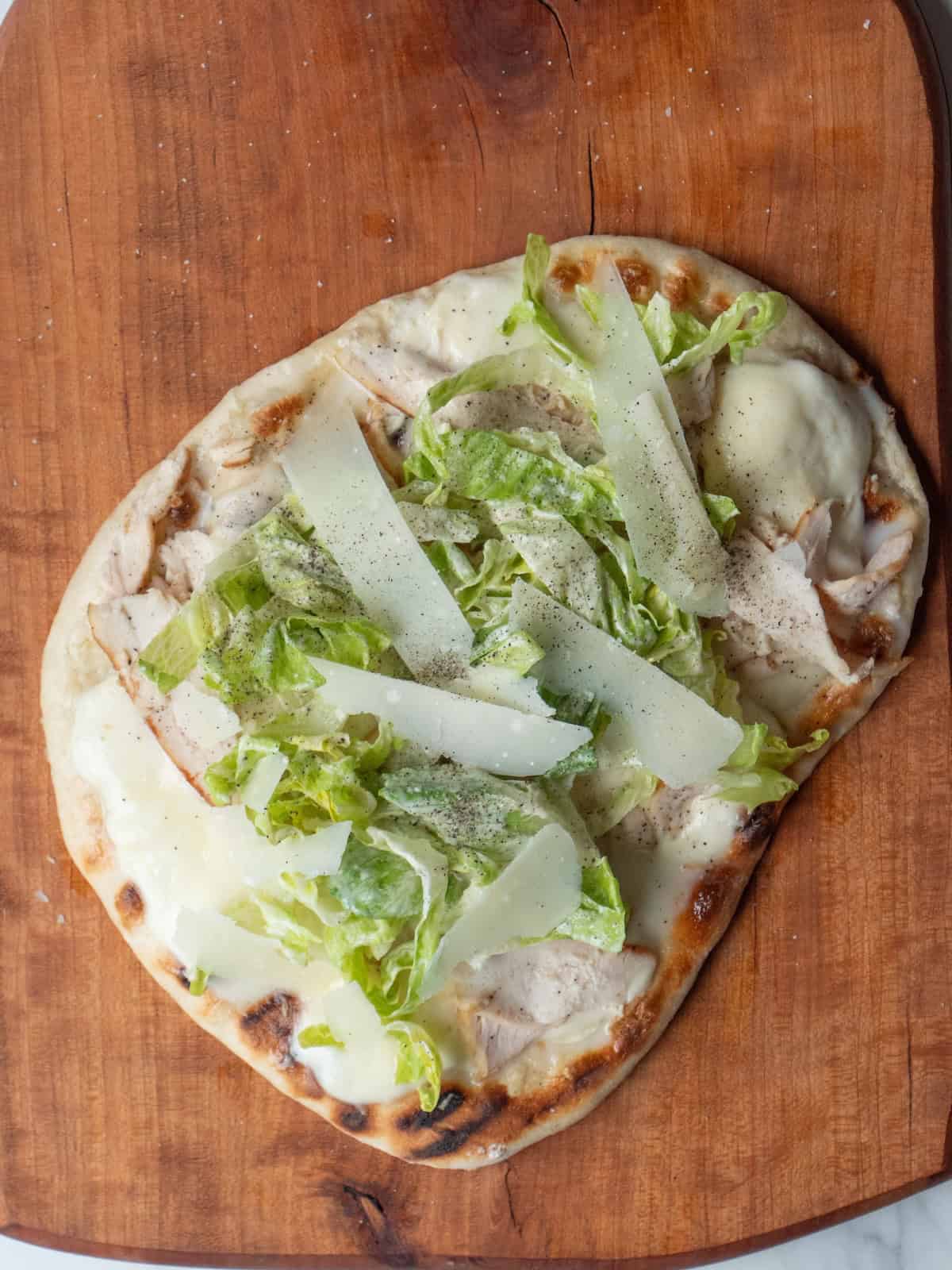 Pizza with cheese and chicken melted on the grill, topped with dressed romaine leaves, salt and pepper, and long strips of parmesan cheese.