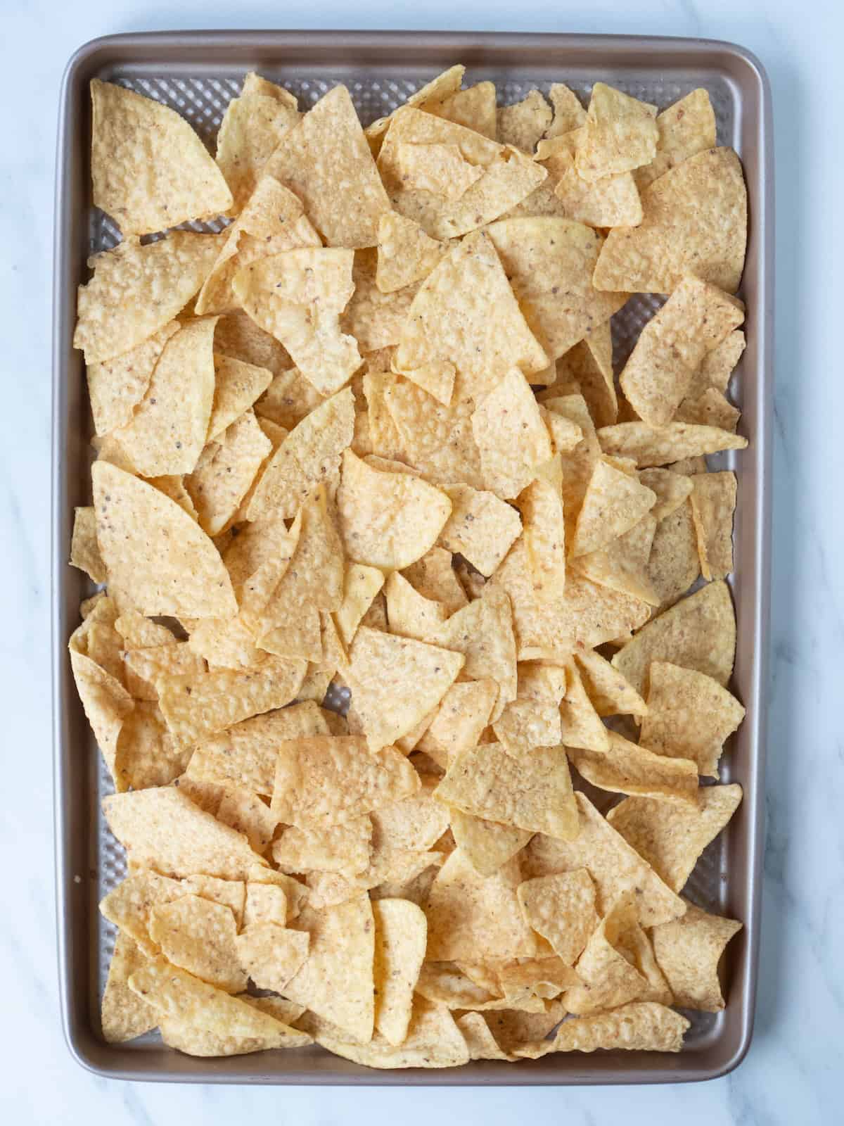 A baking sheet with tortilla chips arranged in a flat layer.