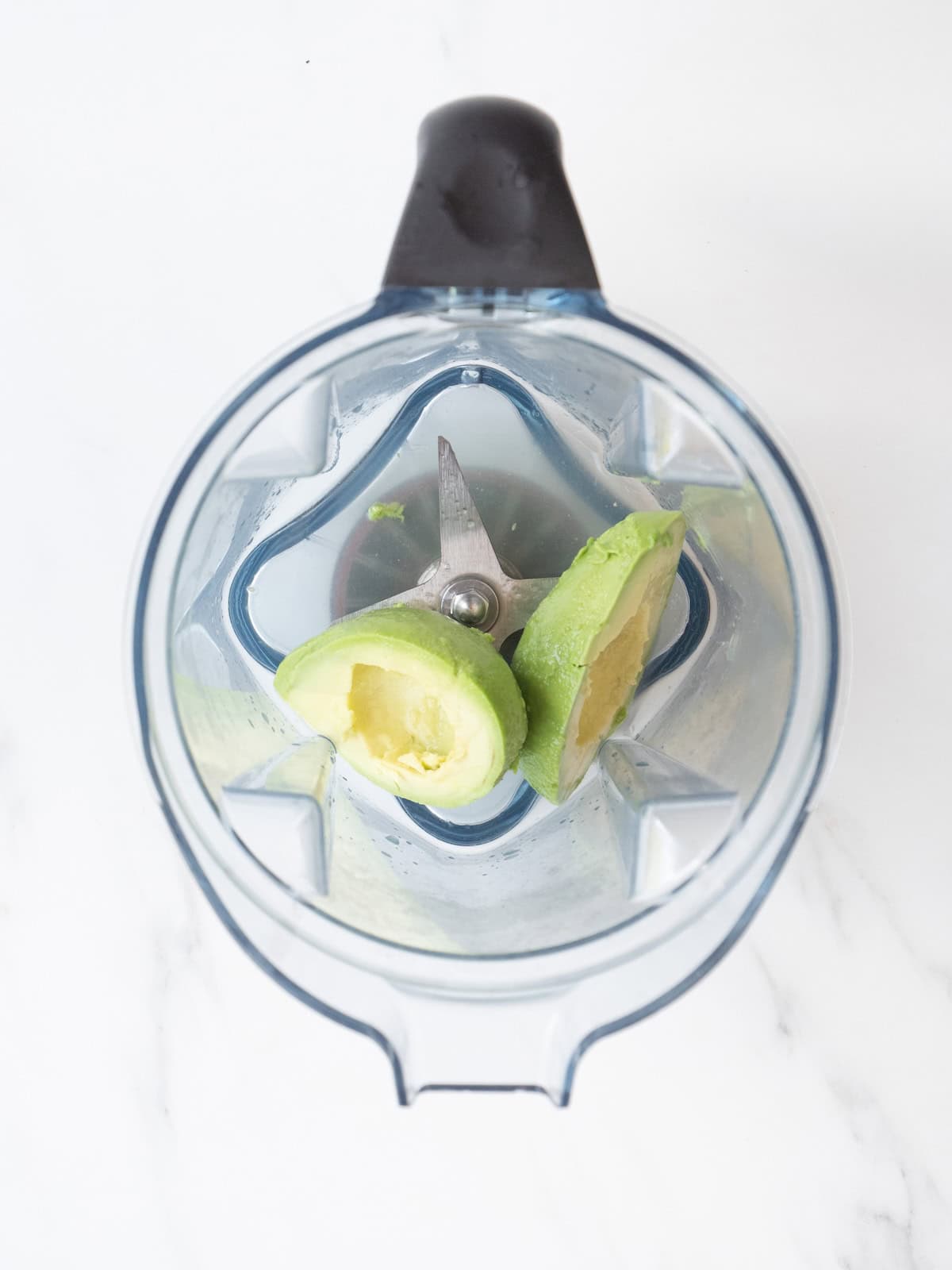A food processor blender jar with avocado and lime juice.
