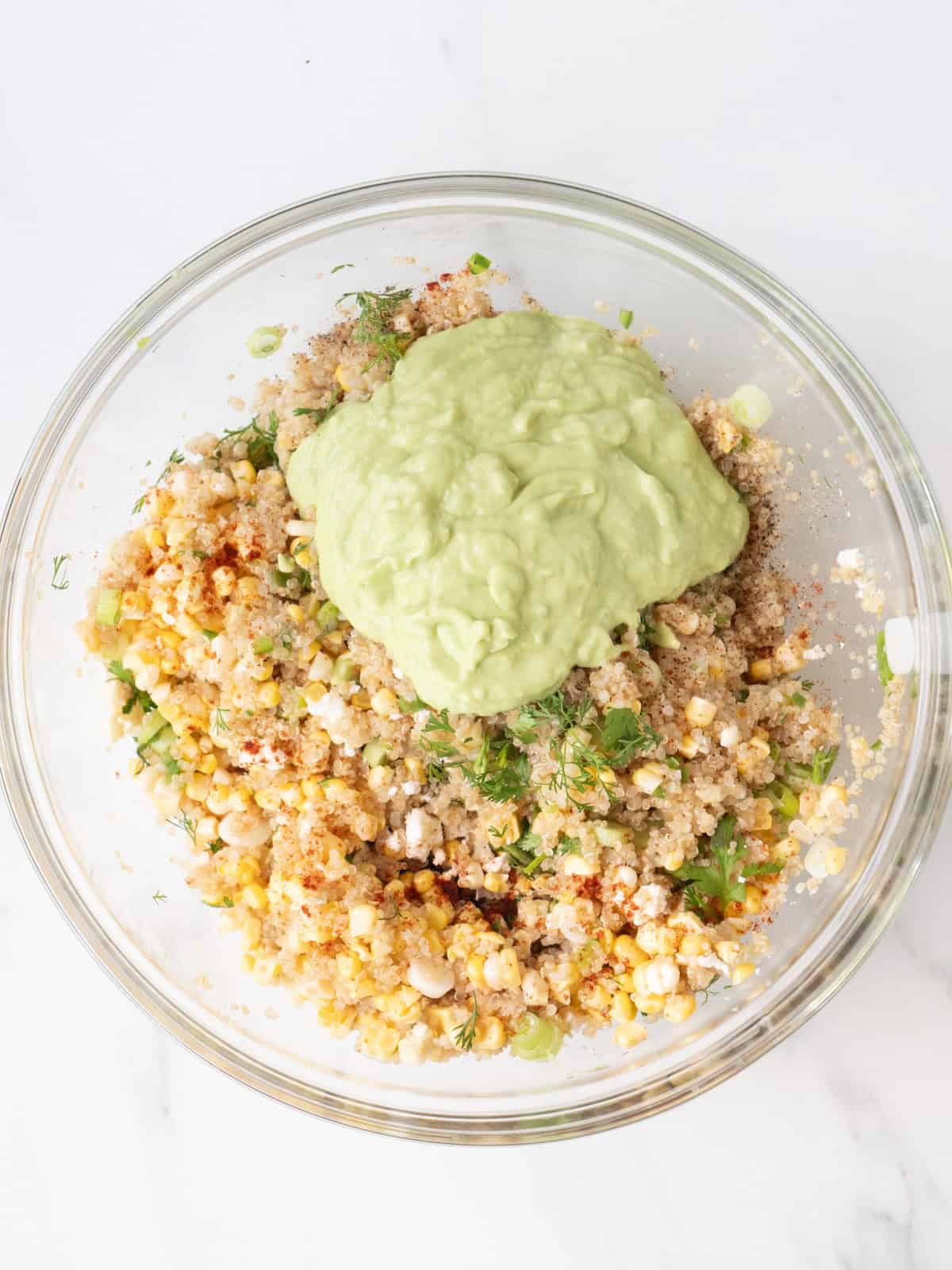 A bowl with mexican corn and quinoa salad being prepared and avocado dressing just added.