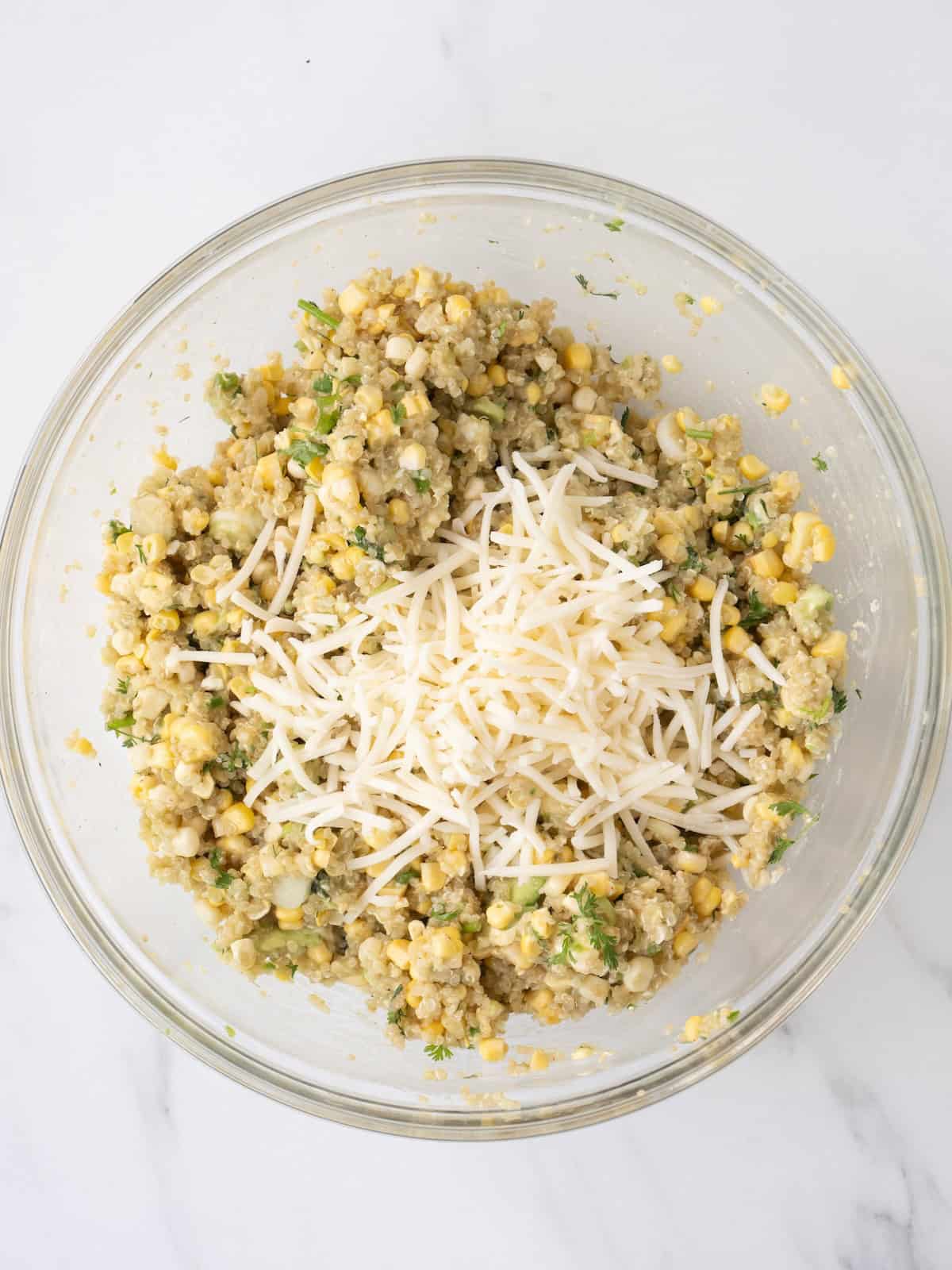 A bowl with mexican corn and quinoa salad topped with shredded Monterey Jack cheese.
