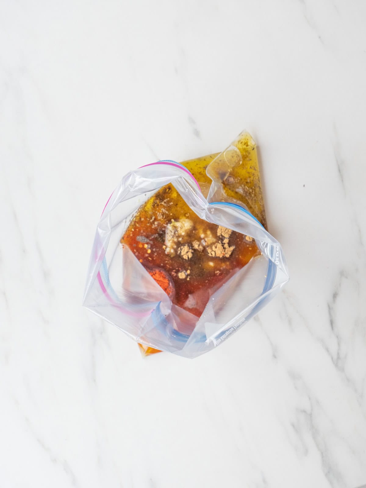 A zip-top bag with marinade ingredients for salmon, lemon, olive oil, garlic, salt and pepper.