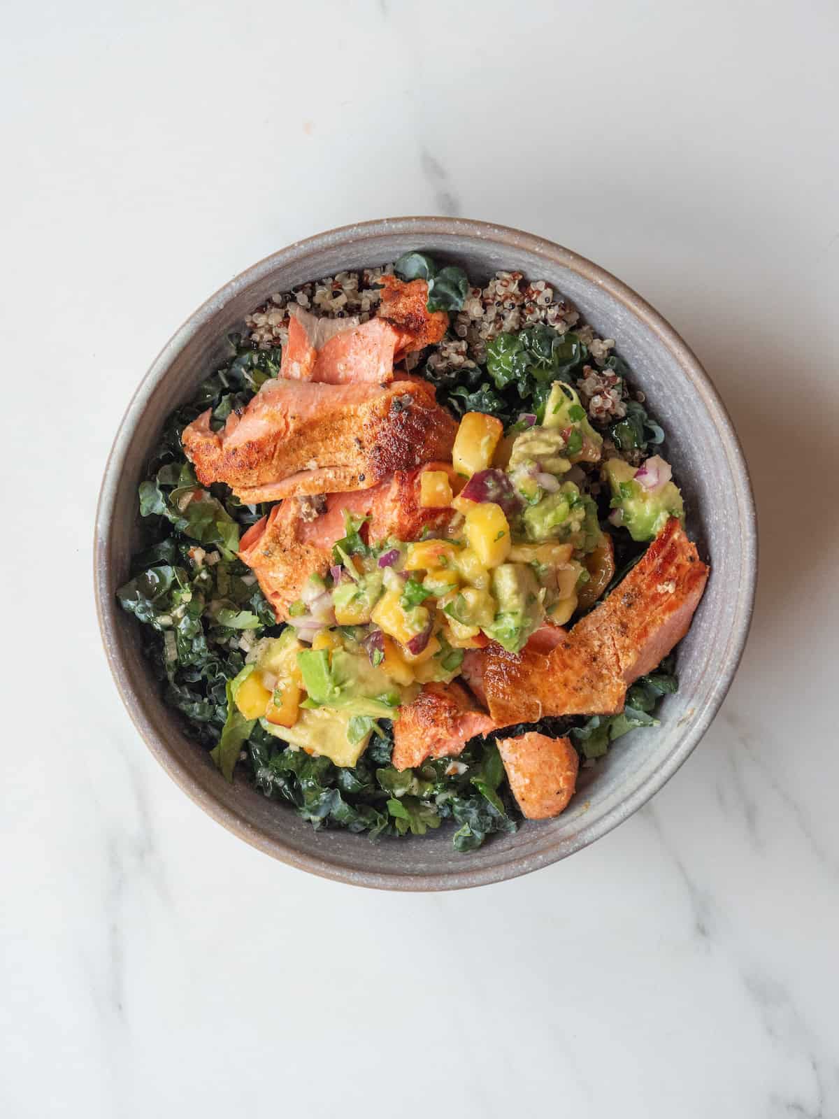 A mixing bowl with a bed of shredded lettuce topped with flaked grilled salmon topped with avocado and fruit mixture.