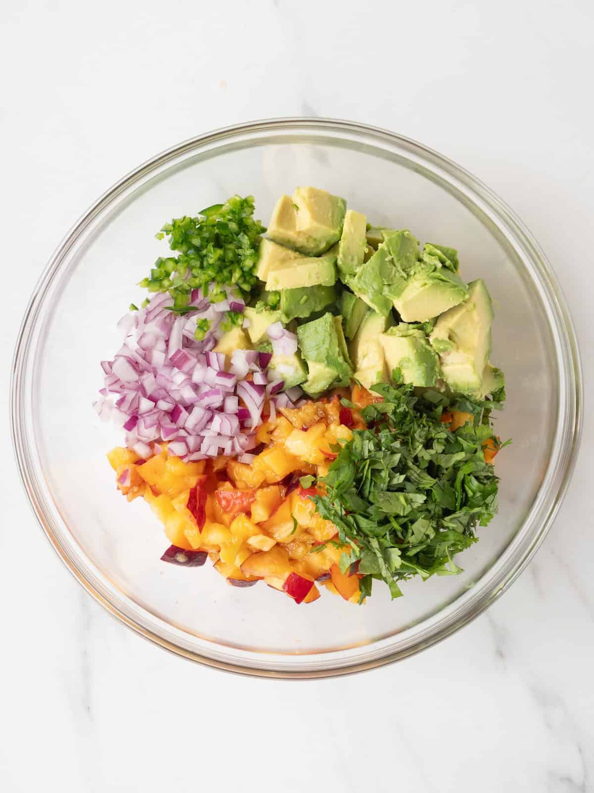 A mixing bowl with chopped avocado, peach, onions, nectarines and cilantro.