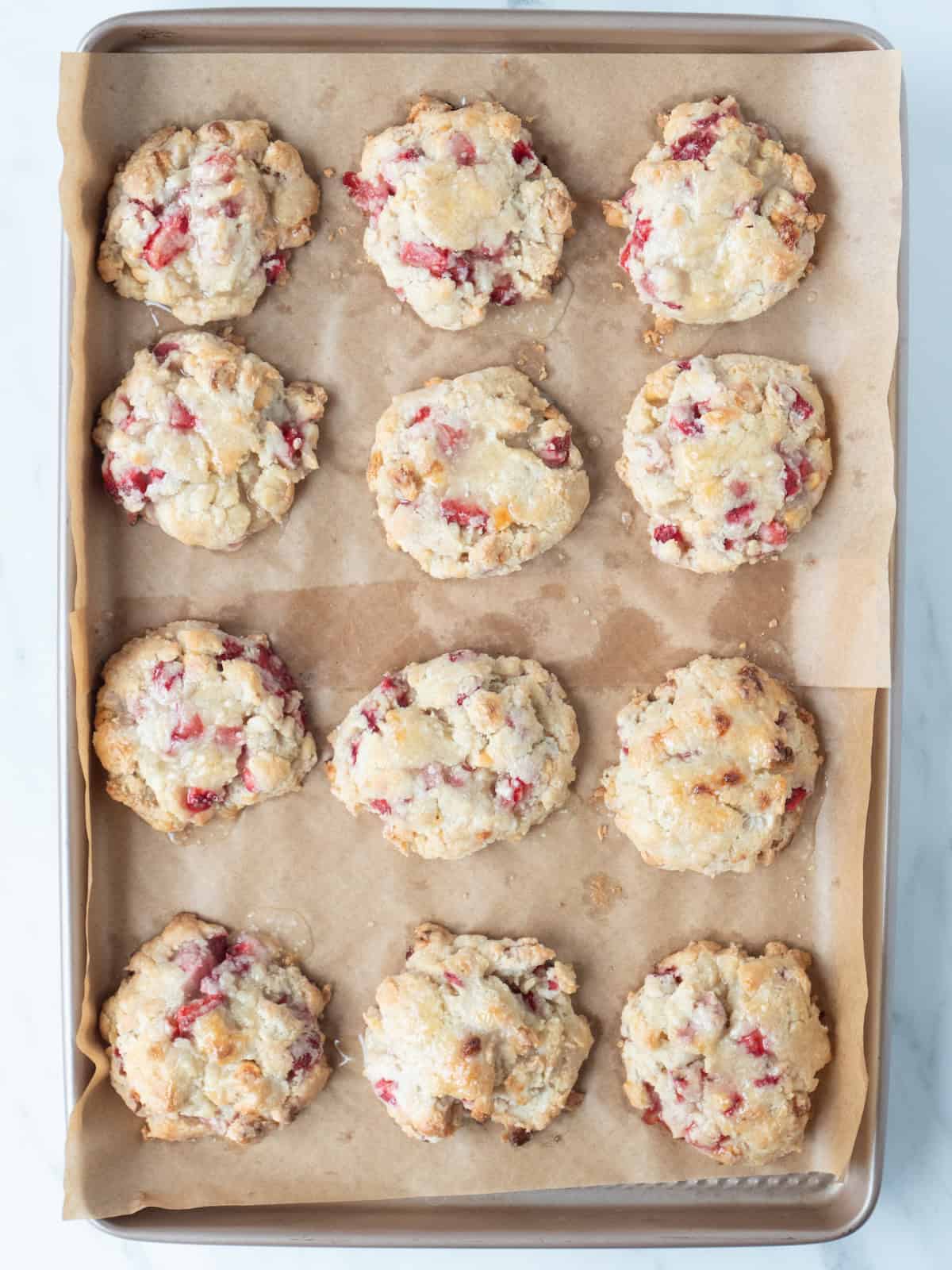 A baking sheet lined with parchment paper with 12 freshly baked strawberry white chocolate scones.
