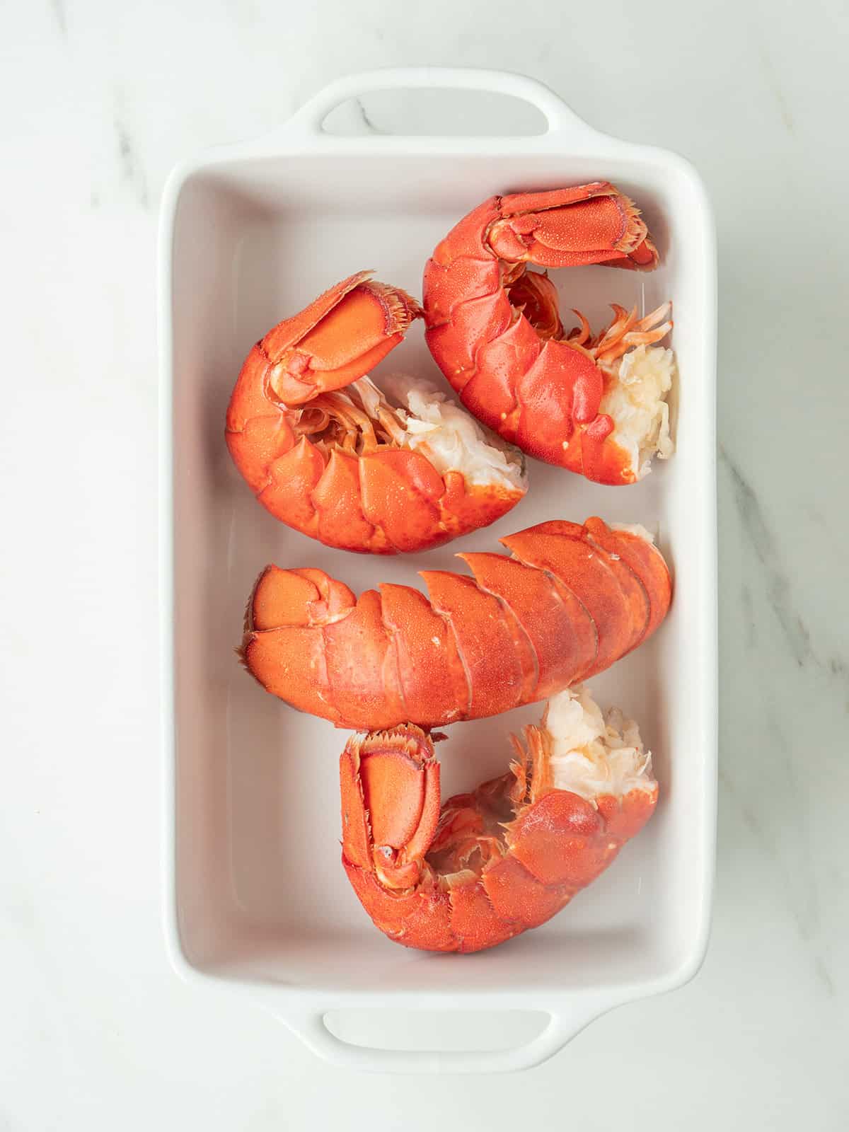 Four cooked lobster tails in dish
