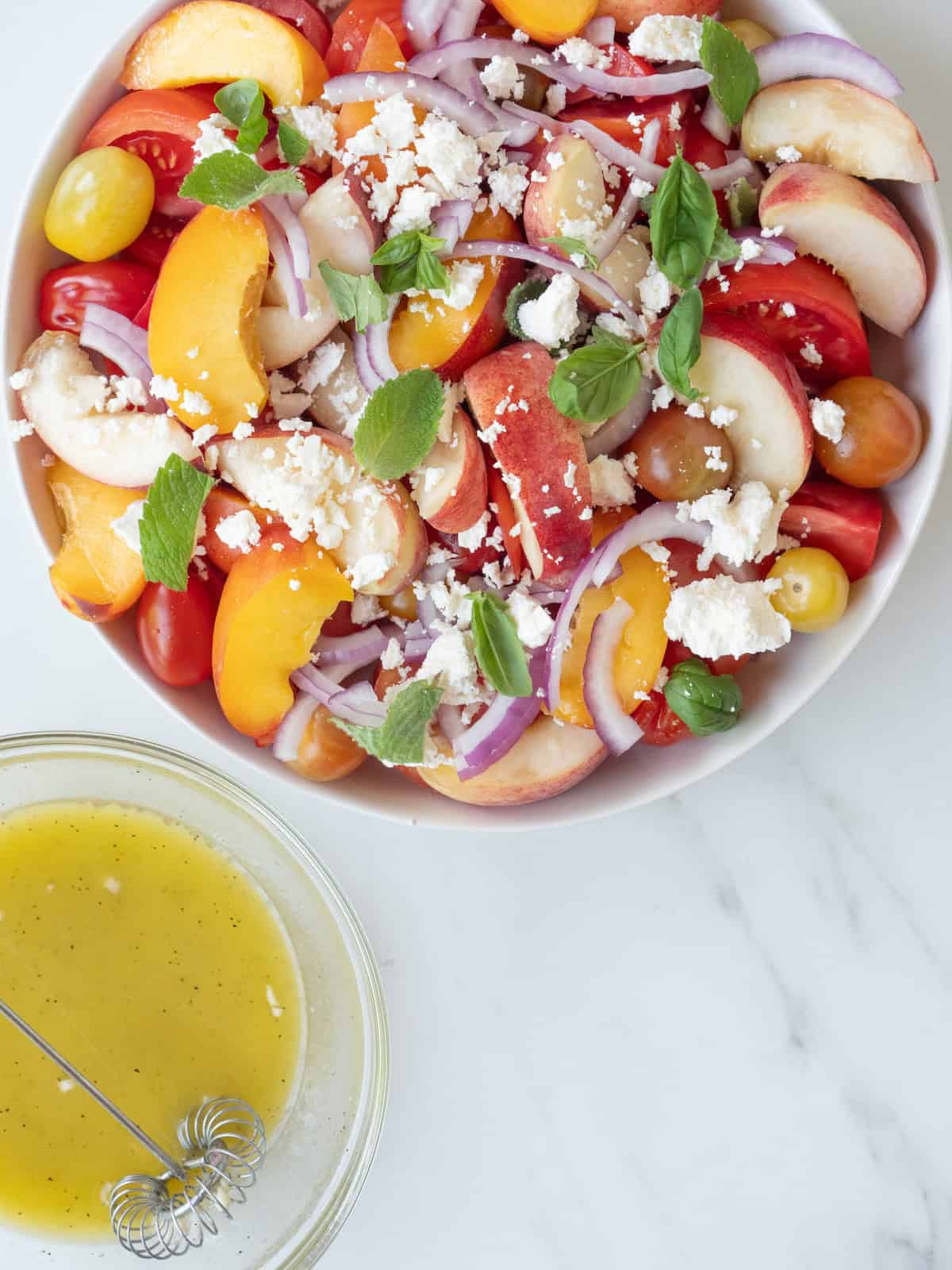 A bowl of stone fruit salad with tomatoes, peaches and nectarines along with a bowl of lemon champagne vinaigrette.
