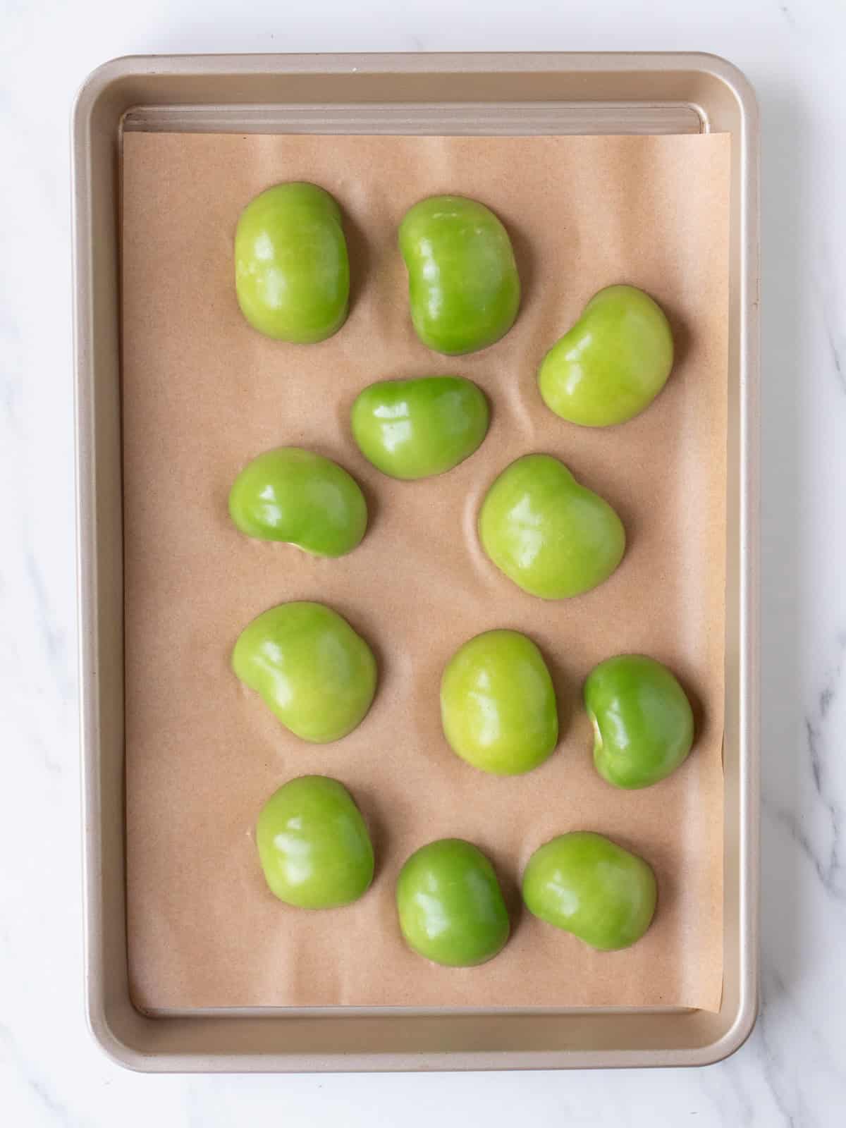 A sheet pan lined with parchment paper, with halved tomatillos, flat side on sheet.