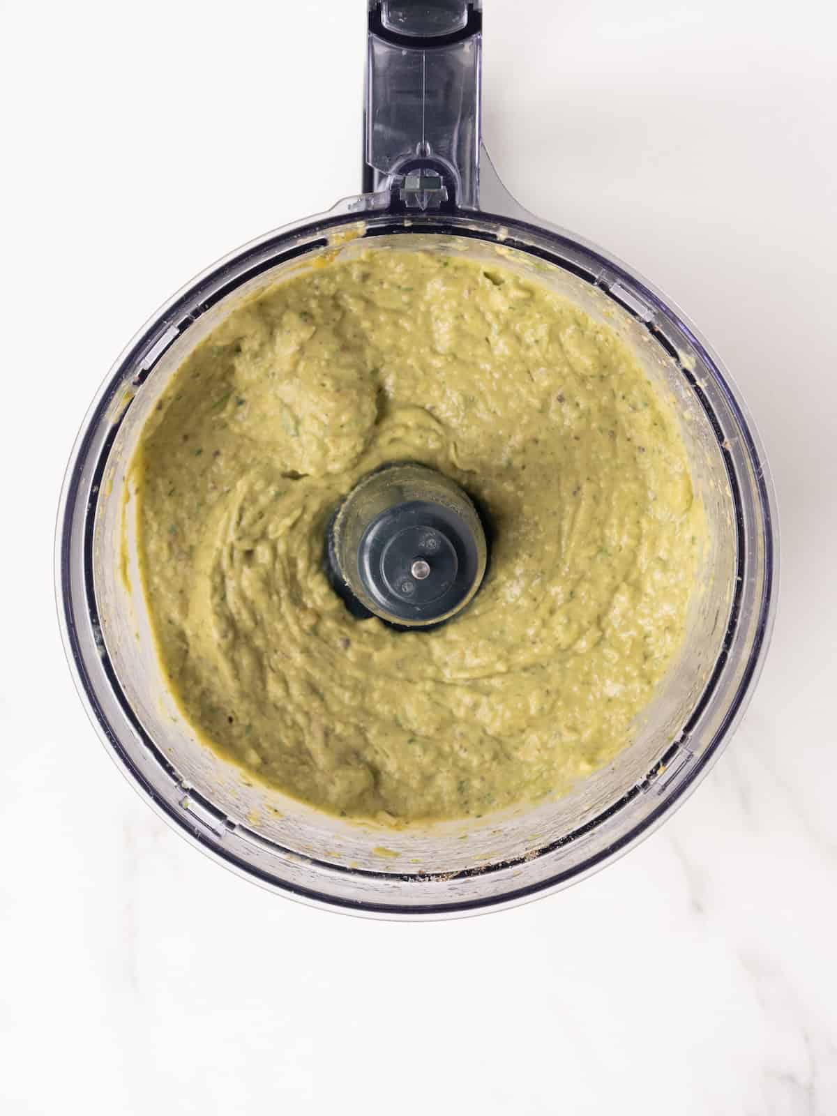 An overhead shot of a food processor jar with tomatillo avocado salsa freshly blended.