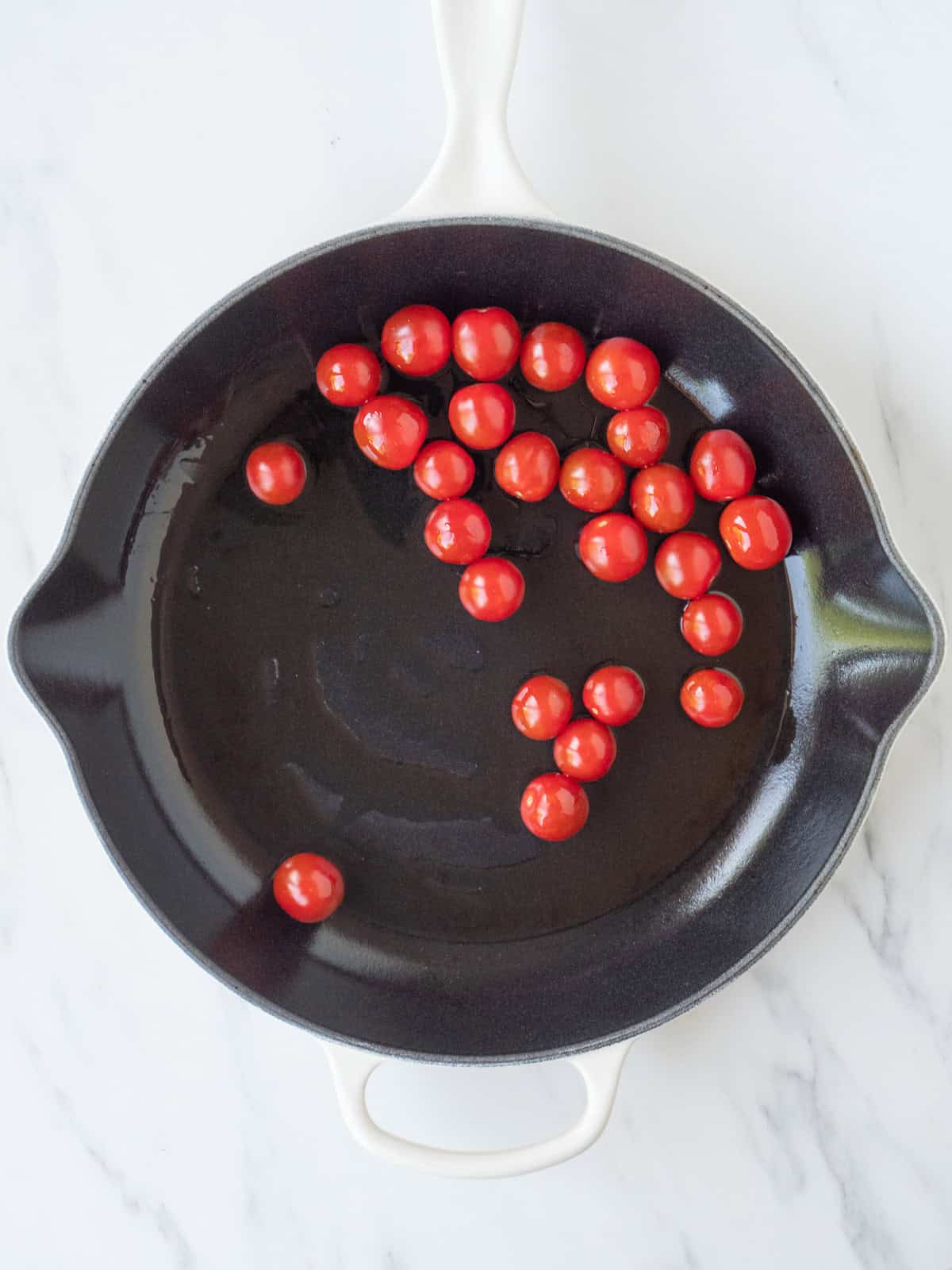 A skillet with olive oil and cherry tomatoes added to it.