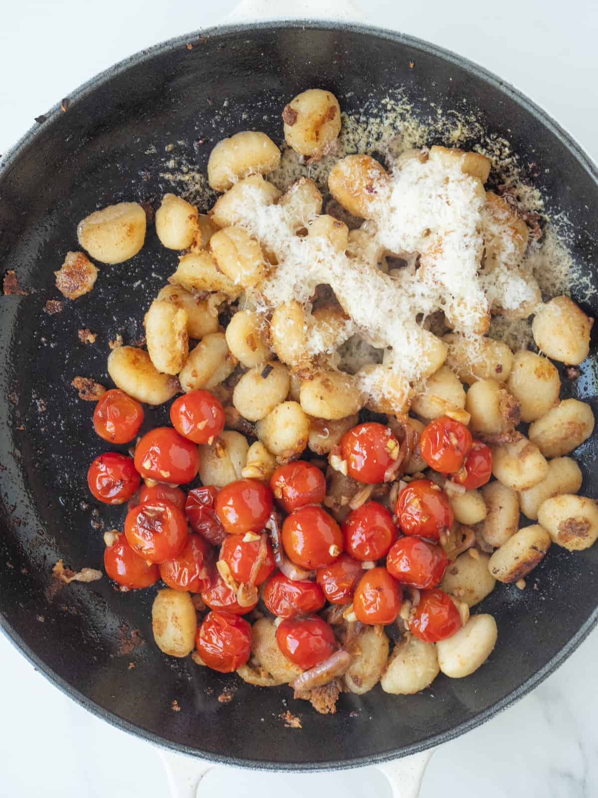 A skillet with gnocchi thats been crisped, along with the blistered cherry tomato mixture and grated parmesan added.