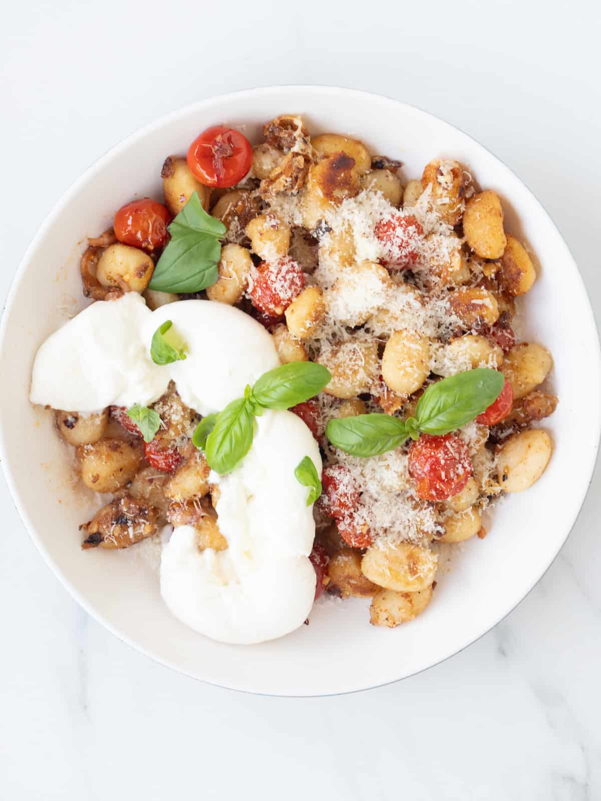 A bowl with tomato basil gnocchi garnished with grated parmesan, basil leaves and burrata.