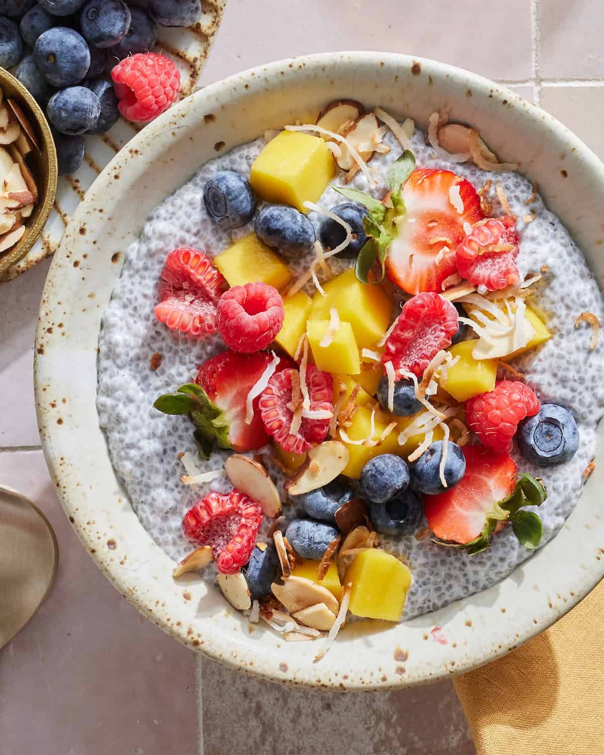 A bowl of chia pudding topped with toasted coconut, sliced almonds, strawberries, raspberries, blueberries and mango.