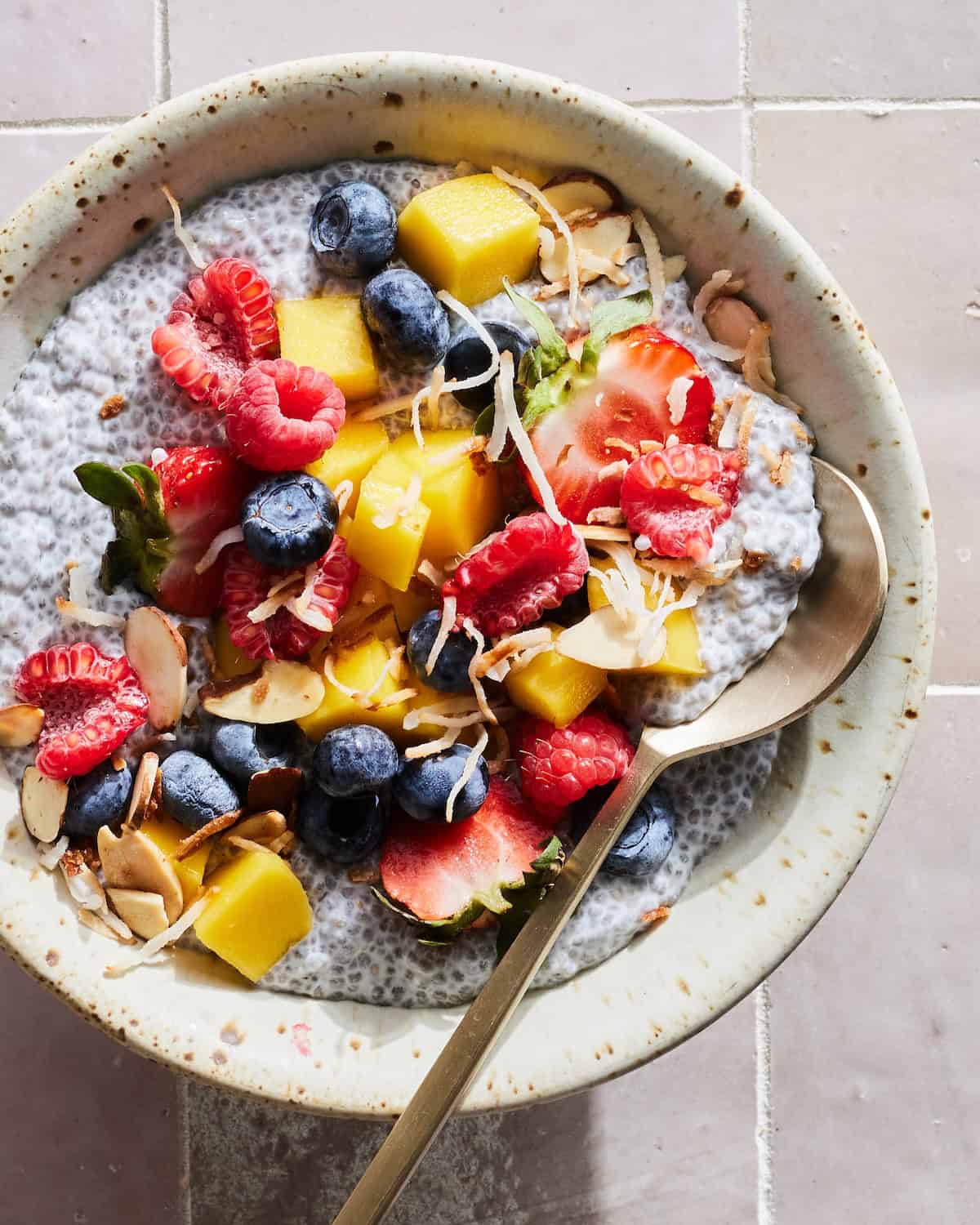 A bowl of chia pudding topped with toasted coconut, sliced almonds, strawberries, raspberries, blueberries and mango.