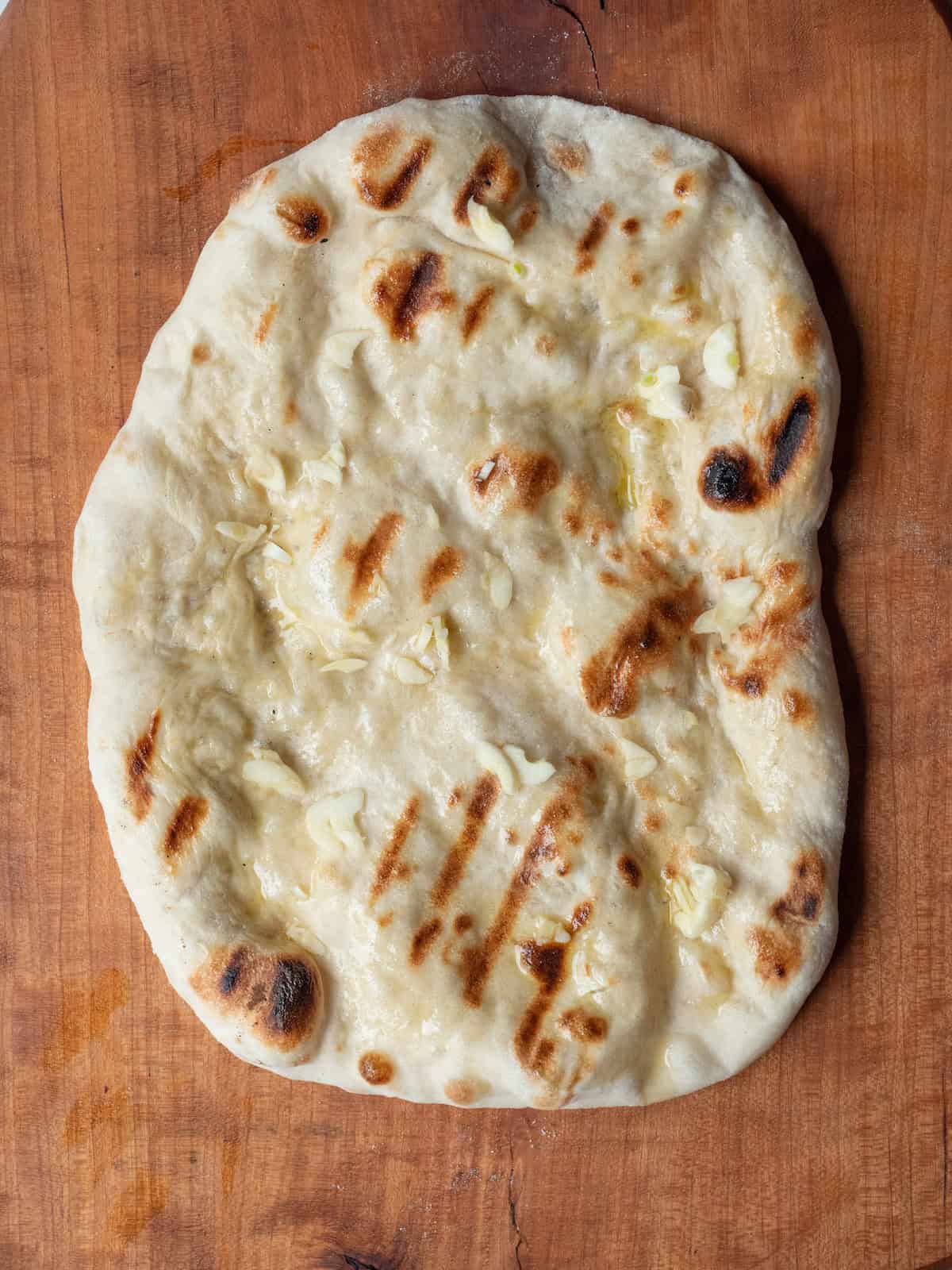 A grilled pizza dough brushed with olive oil and sprinkled with garlic.