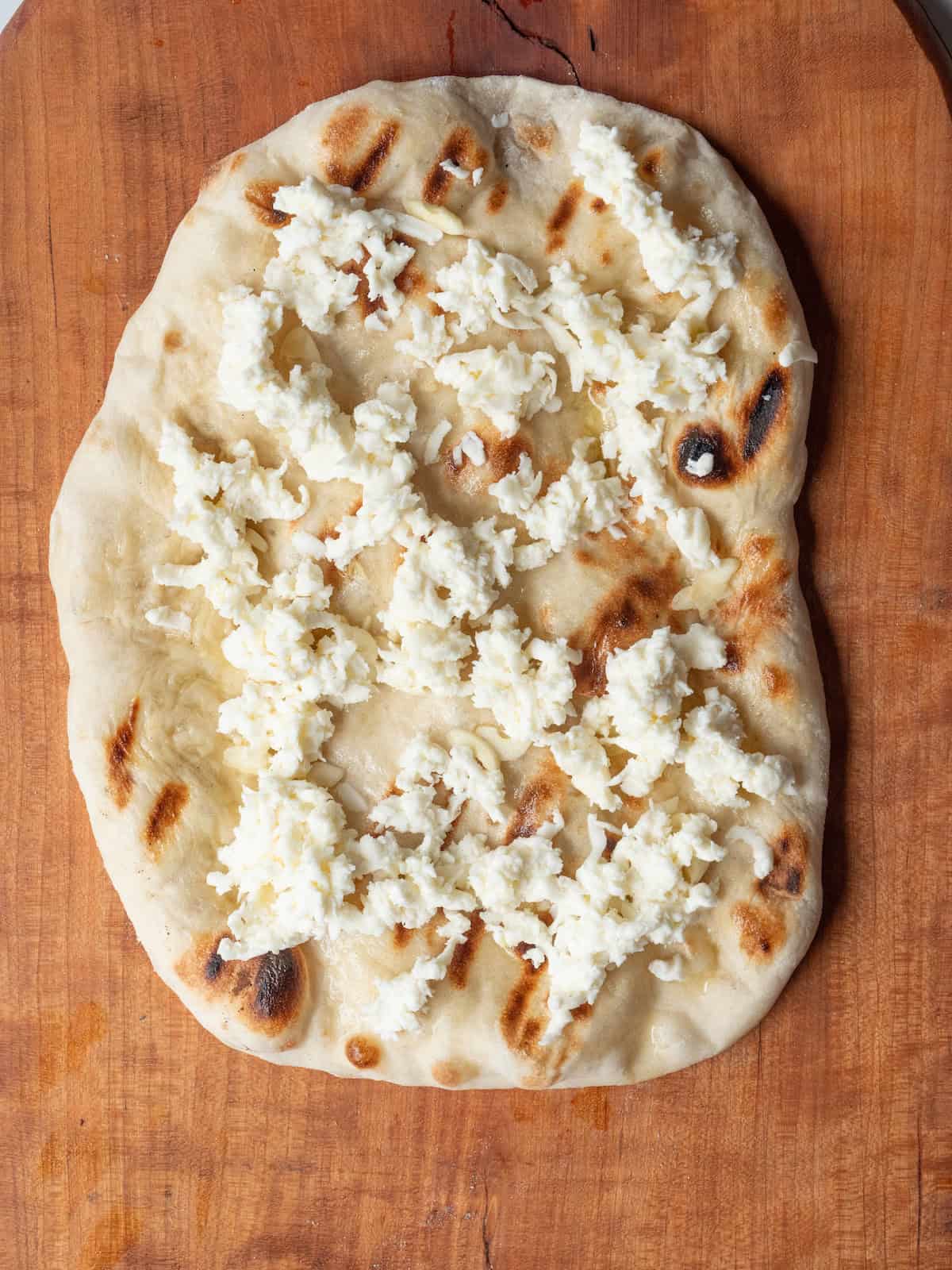 A grilled pizza dough with mozzarella torn and spread all over it.