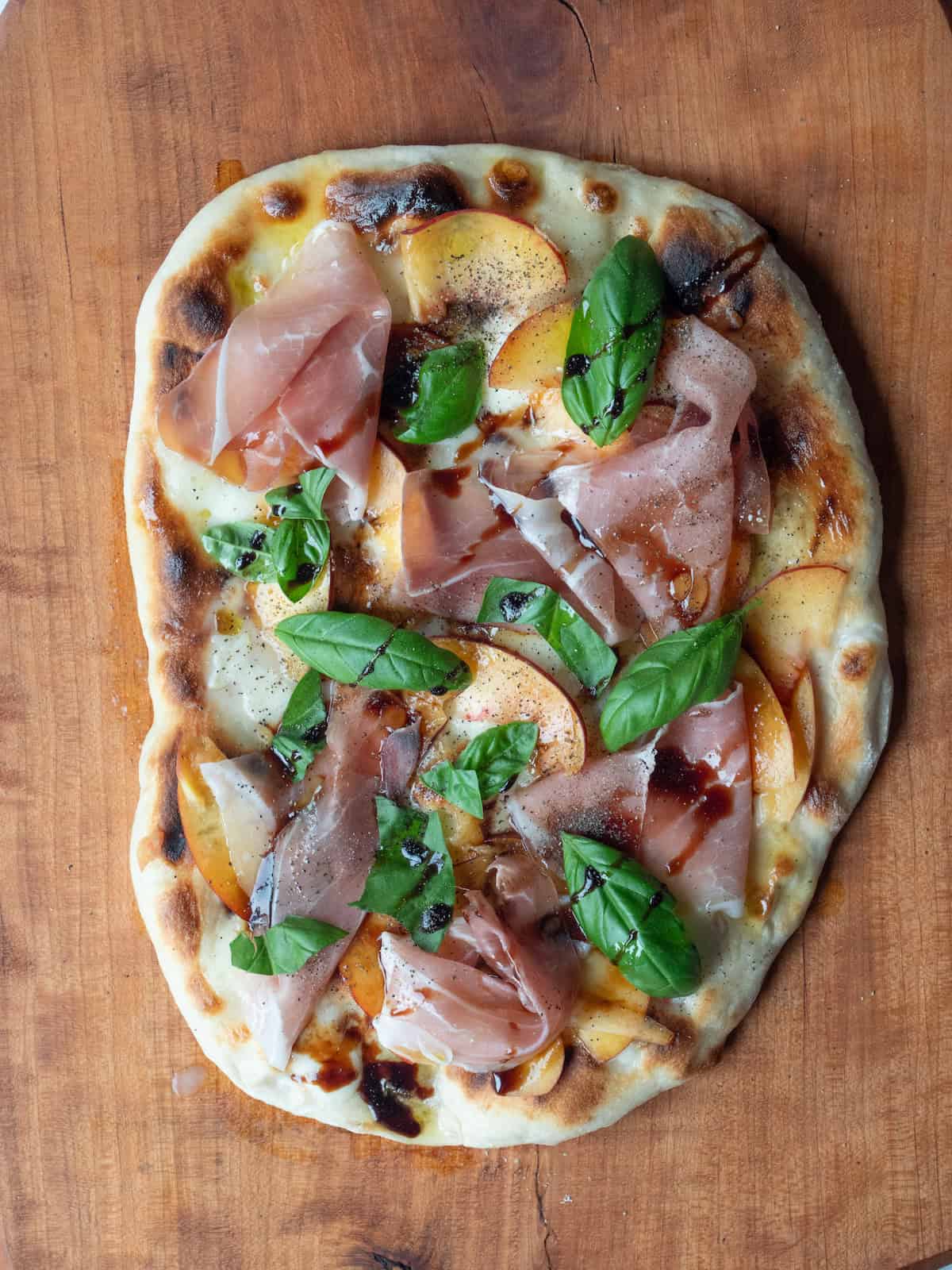 A grilled peach and prosciutto pizza drizzled with olive oil and reduced balsamic and seasoned with salt and pepper.