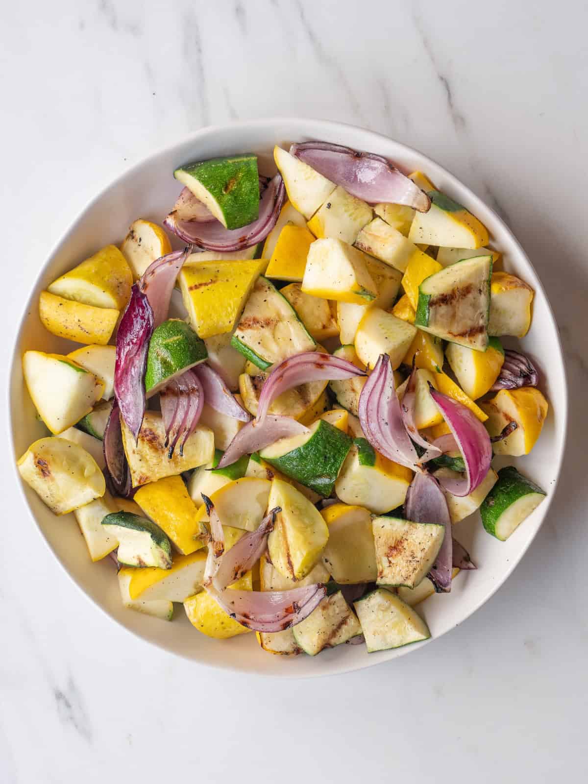 A large bowl of cubed and grilled yellow squash, zucchini, patty pan squash and red onions.