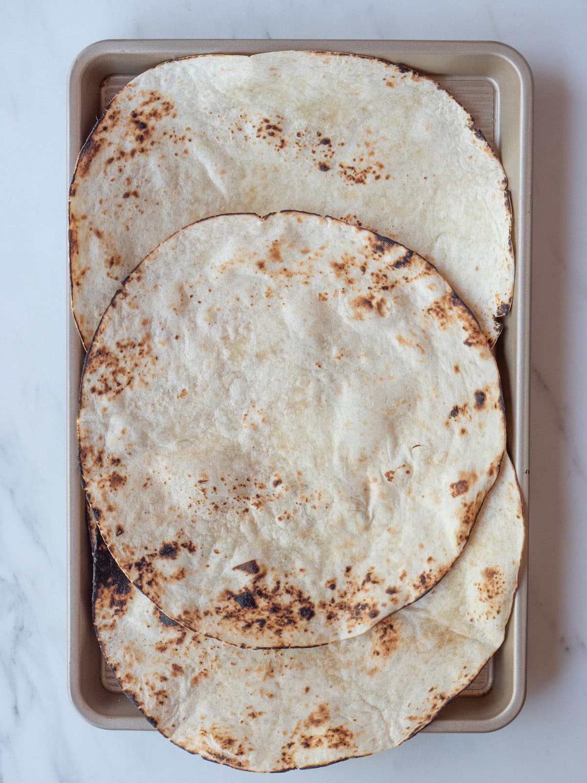 A baking sheet with tortillas that have been charred on an open flame on the stove to warm them up.