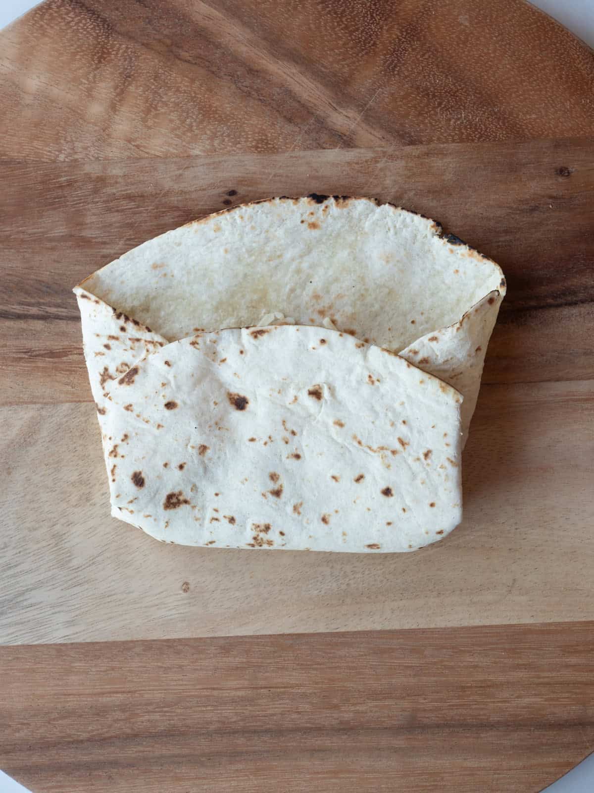 A wooden board with a burrito that has had its fillings added and halfway into being folded into a burrito.