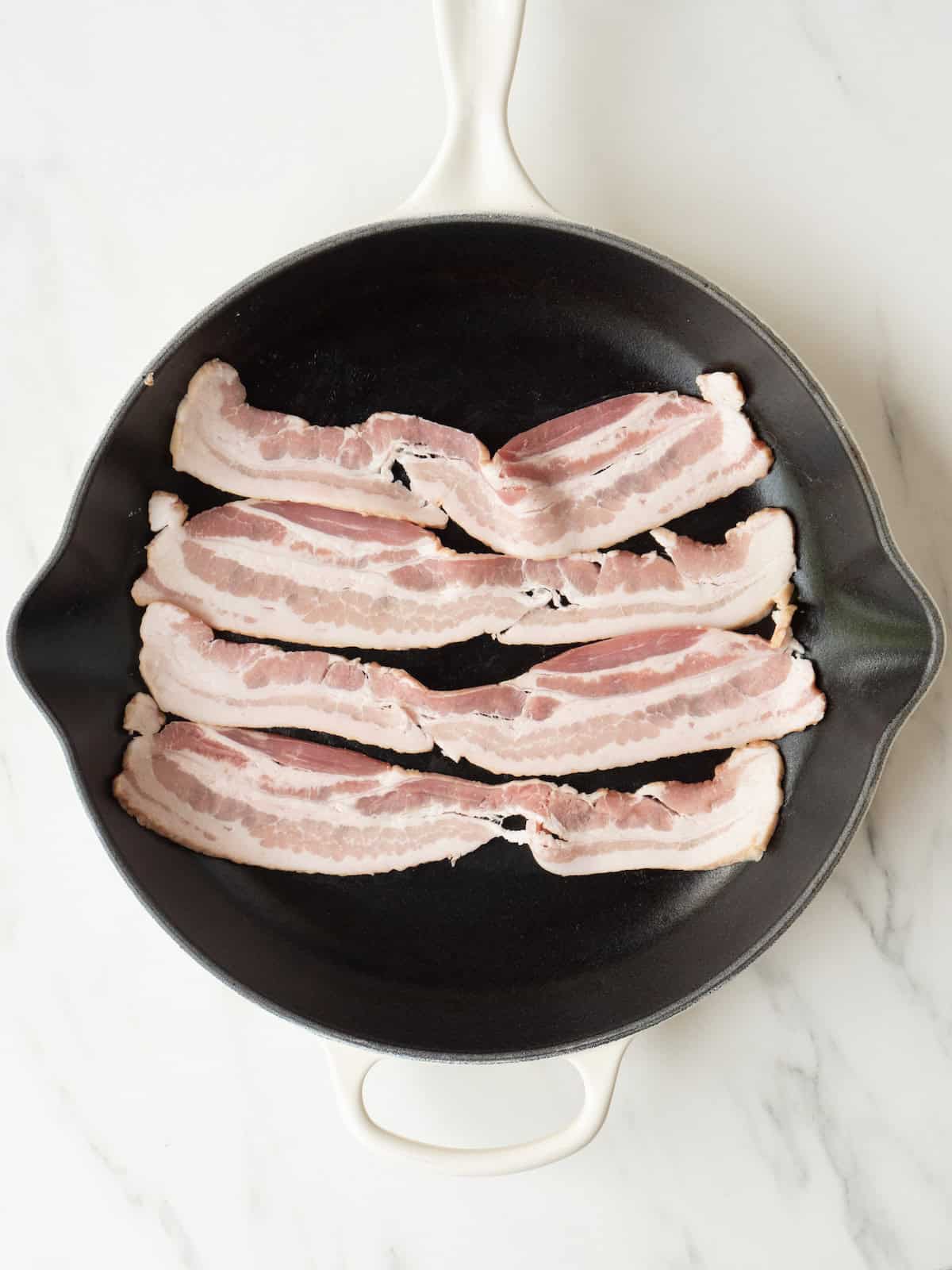 A skillet with bacon being cooked.