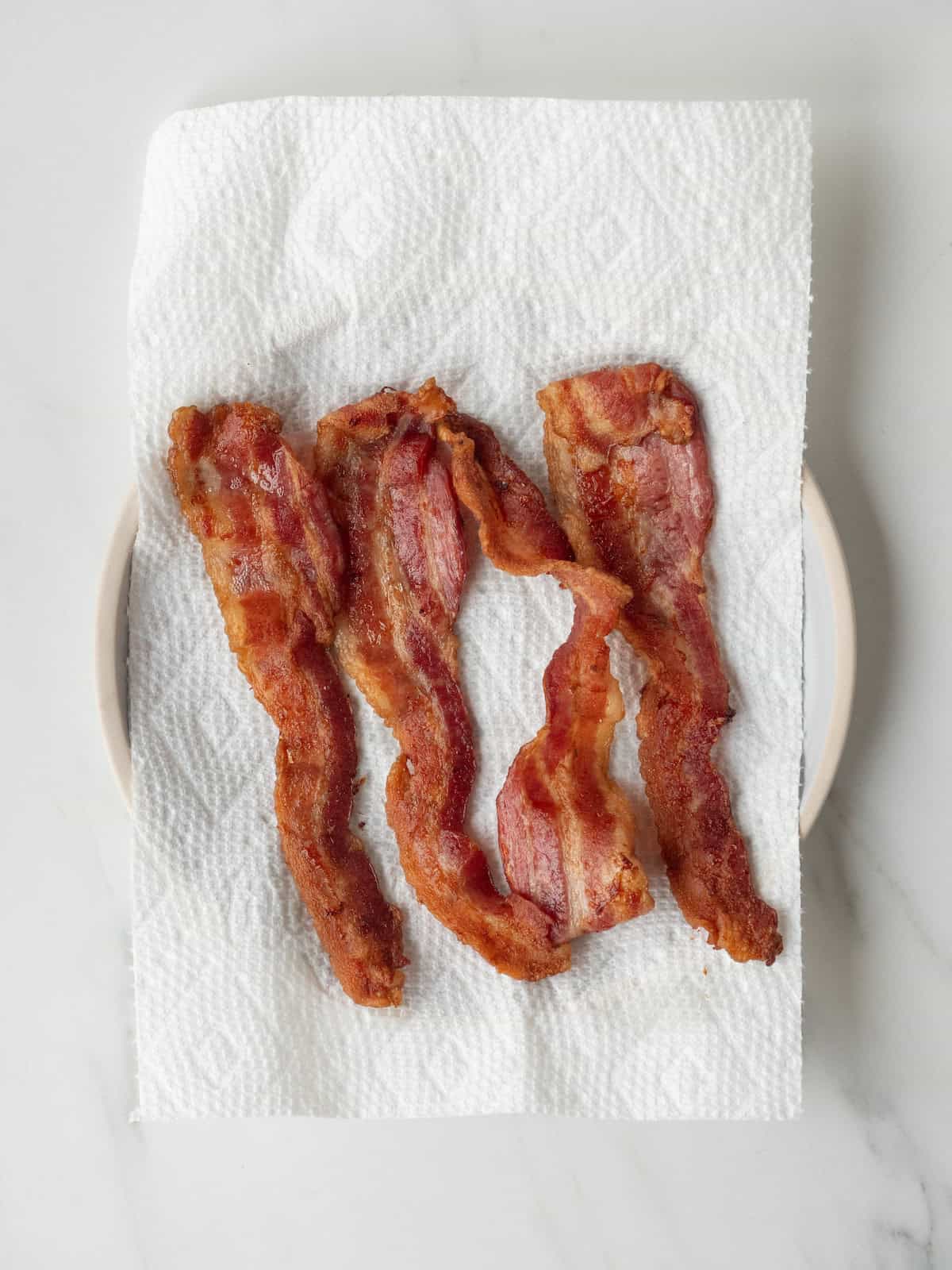 A plate lined with tissue with freshly cooked bacon on it.