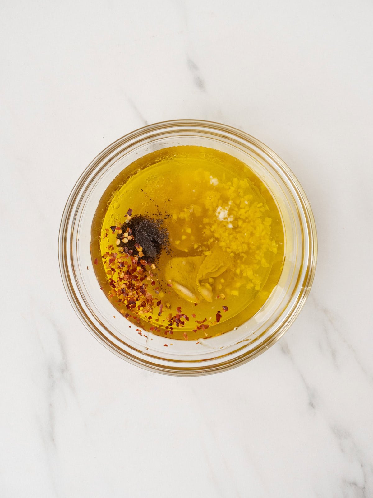 A glass mixing bowl with all ingredients for lemon champagne vinaigrette ready to be mixed.