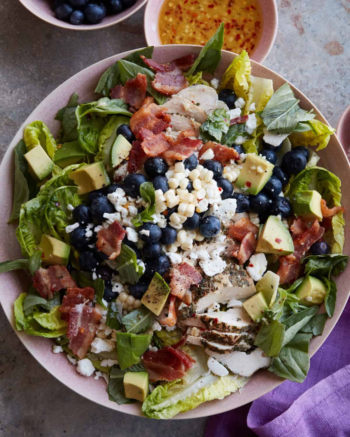 A bowl of a summery grilled chicken power salad with blueberries, corn, avocado and bacon.